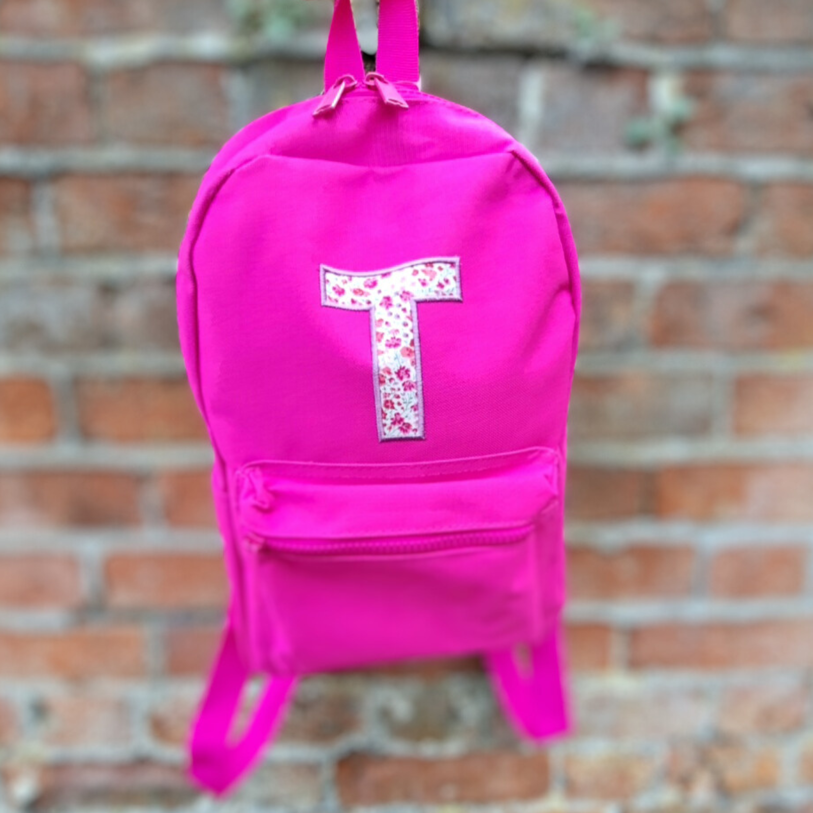 image of a fuchsia pink ruck sack that has been personalised with an initial T which is appliqued onto the front of the bag in Liberty print fabric