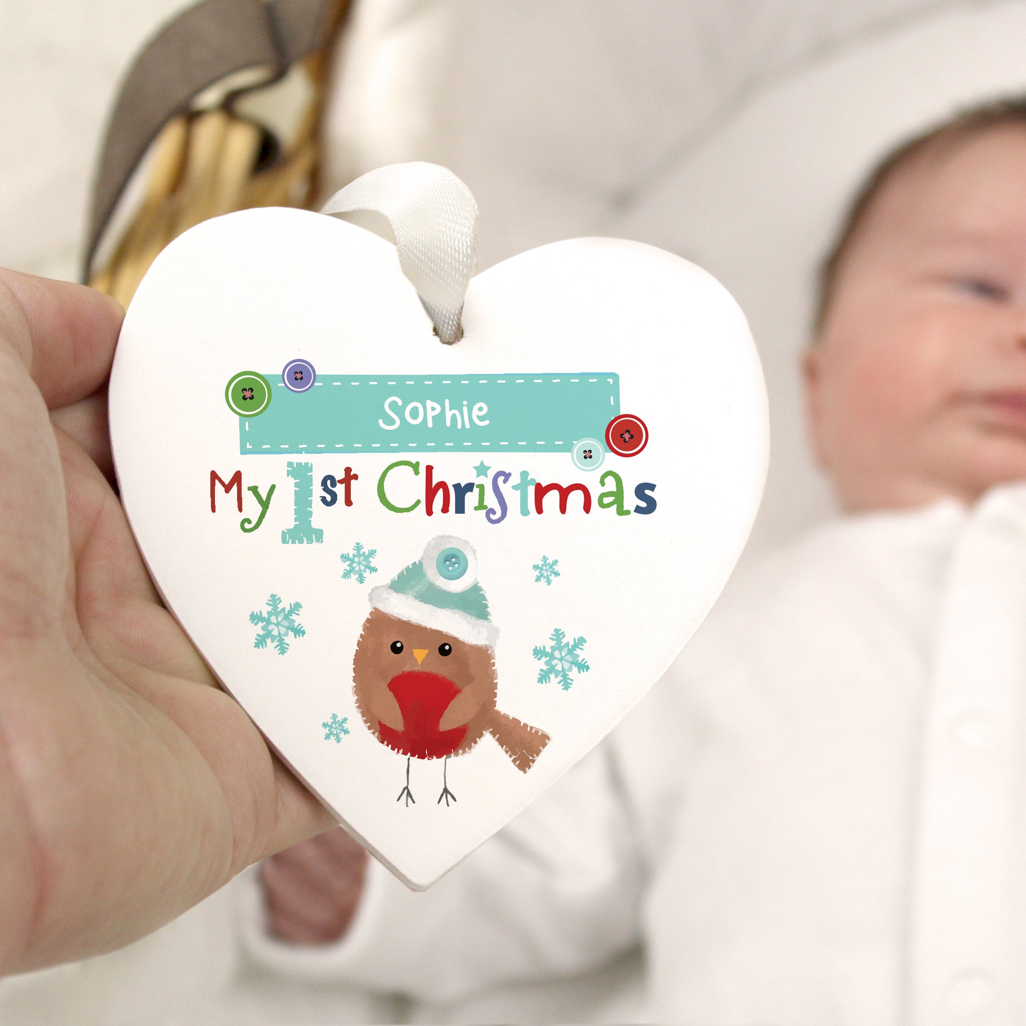Personalised white wooden heart shaped Christmas decoration featuring an image of a hand-painted robin and the text 'My 1st Christmas' in bright letters. The decoration can be personalised with a name of your choice up to 12 characters.