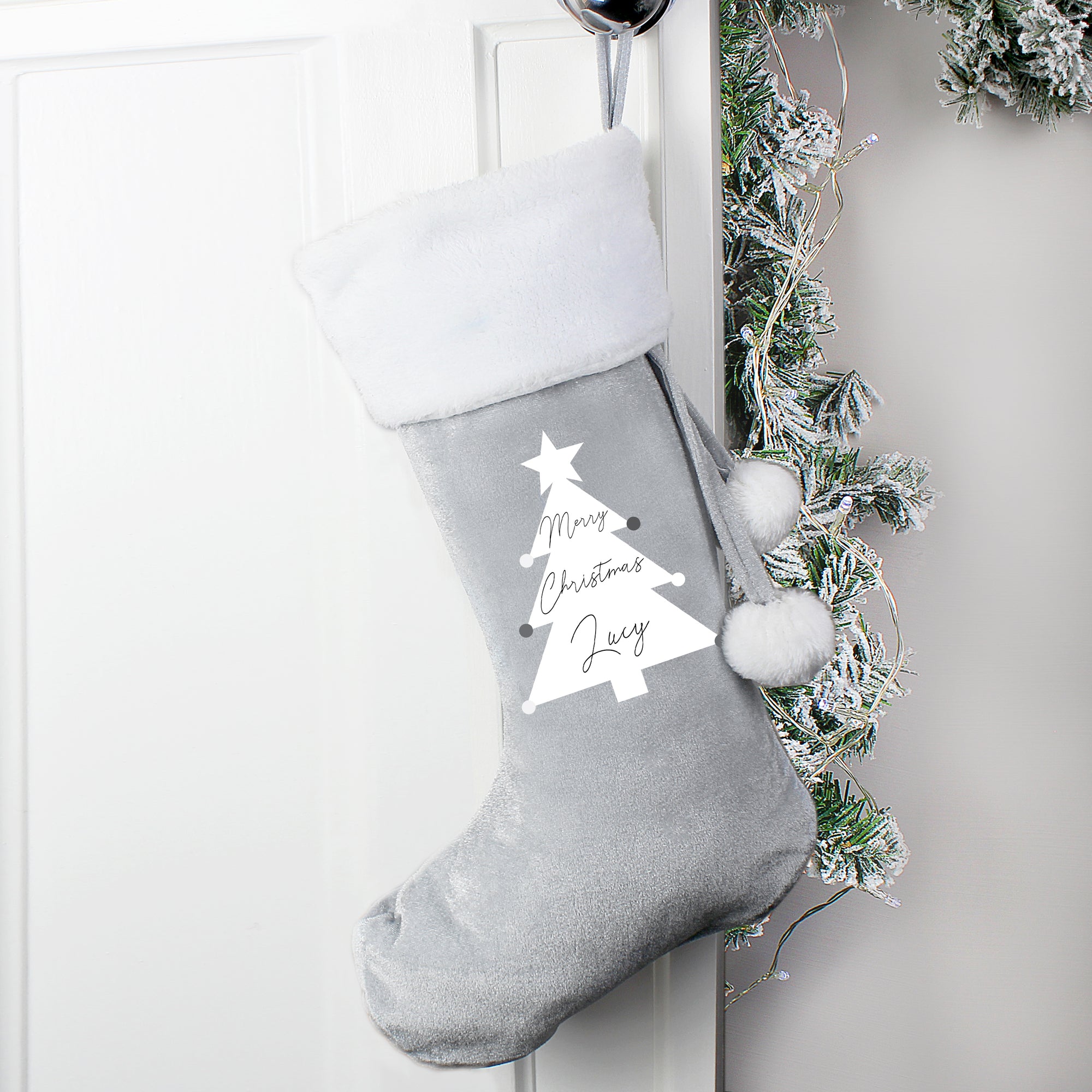 Personalised silver velvet Christmas stocking with a white plush trim and a loop to hang it from. The front of the stocking features an image of a white Christmas tree and the wording 'Merry Christmas' printed inside the tree in a black modern cursive font. You can then add a name of your choice which will be printed directly below the wording in the same black font.