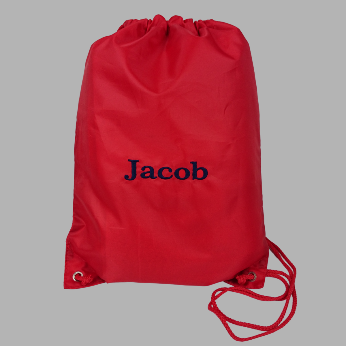Personalised PE or swimming bag shown in red with a name embroidered in navy blue thread.