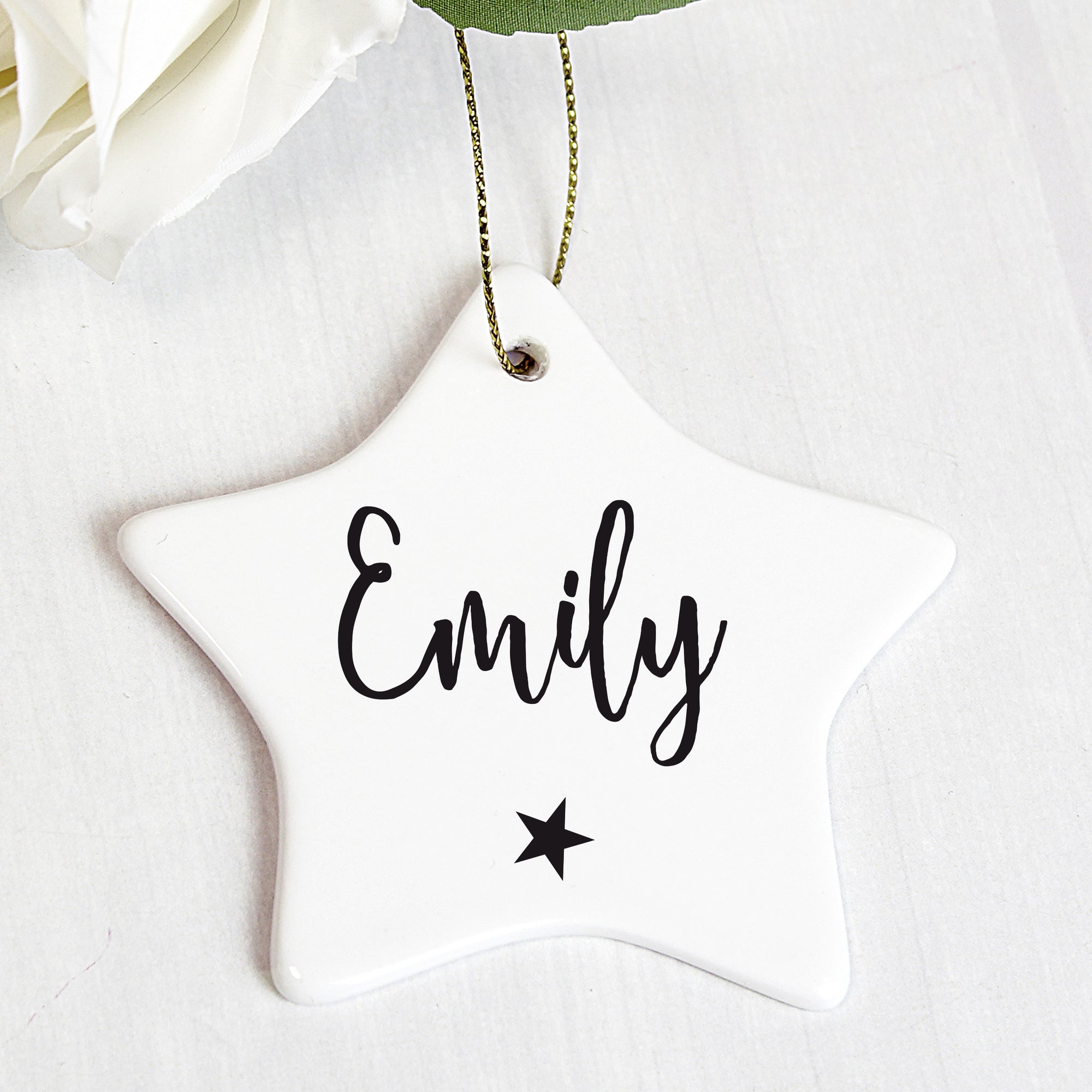 Personalised white ceramic star shaped Christmas decoration that comes with a string ready to hang. The front of the decoration can be personalised with a name of up to 12 characters which will be printed in a black modern hand written style font and there is a small black star printed below the name.