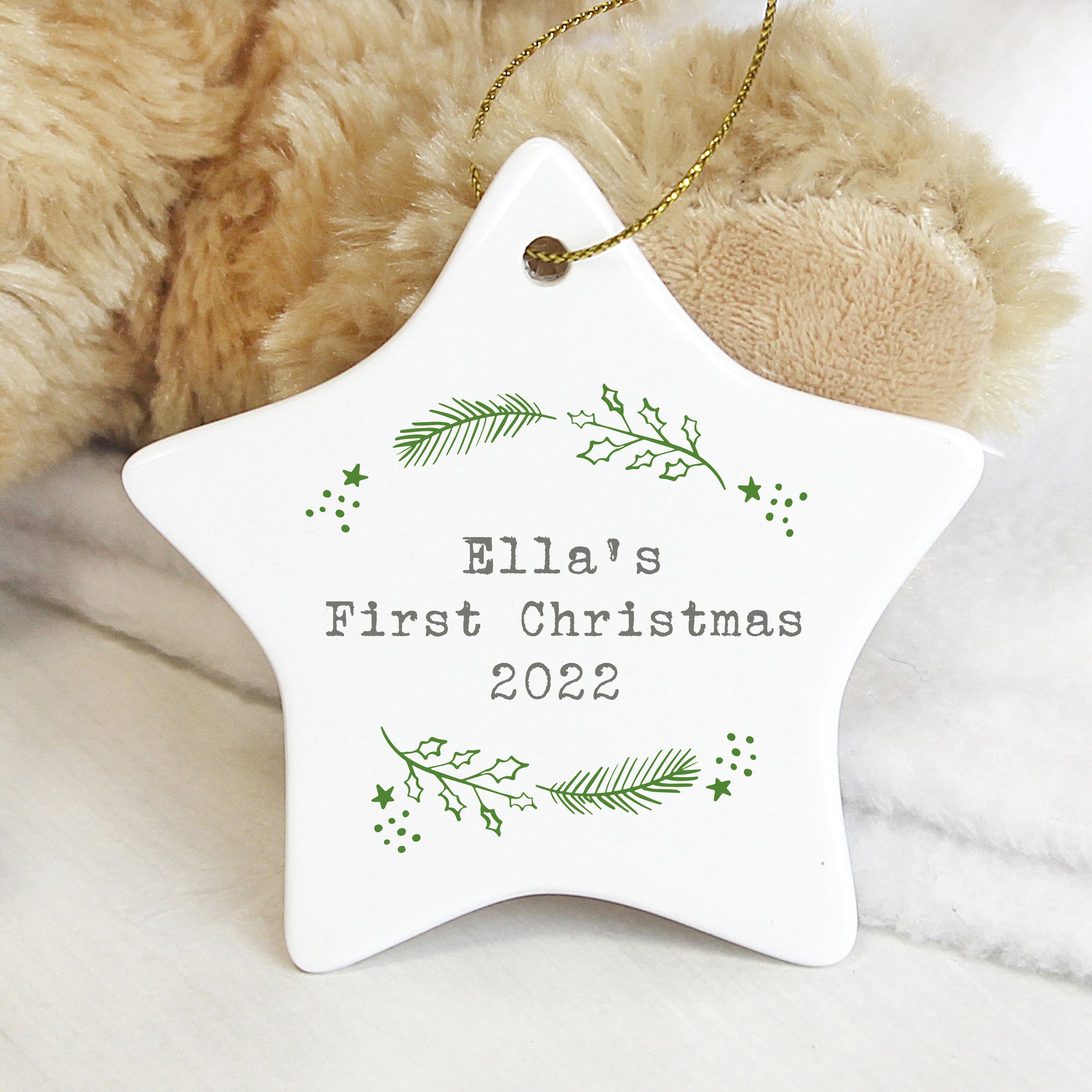 Image of a white ceramic star Christmas decoration which can be personalised with your own text or message over up to 3 lines. The star features a green holly and Christmas fir branch design and the personalisation will be printed in the centre of the star in a grey type writer effect font. The star comes with a string to hang it from.