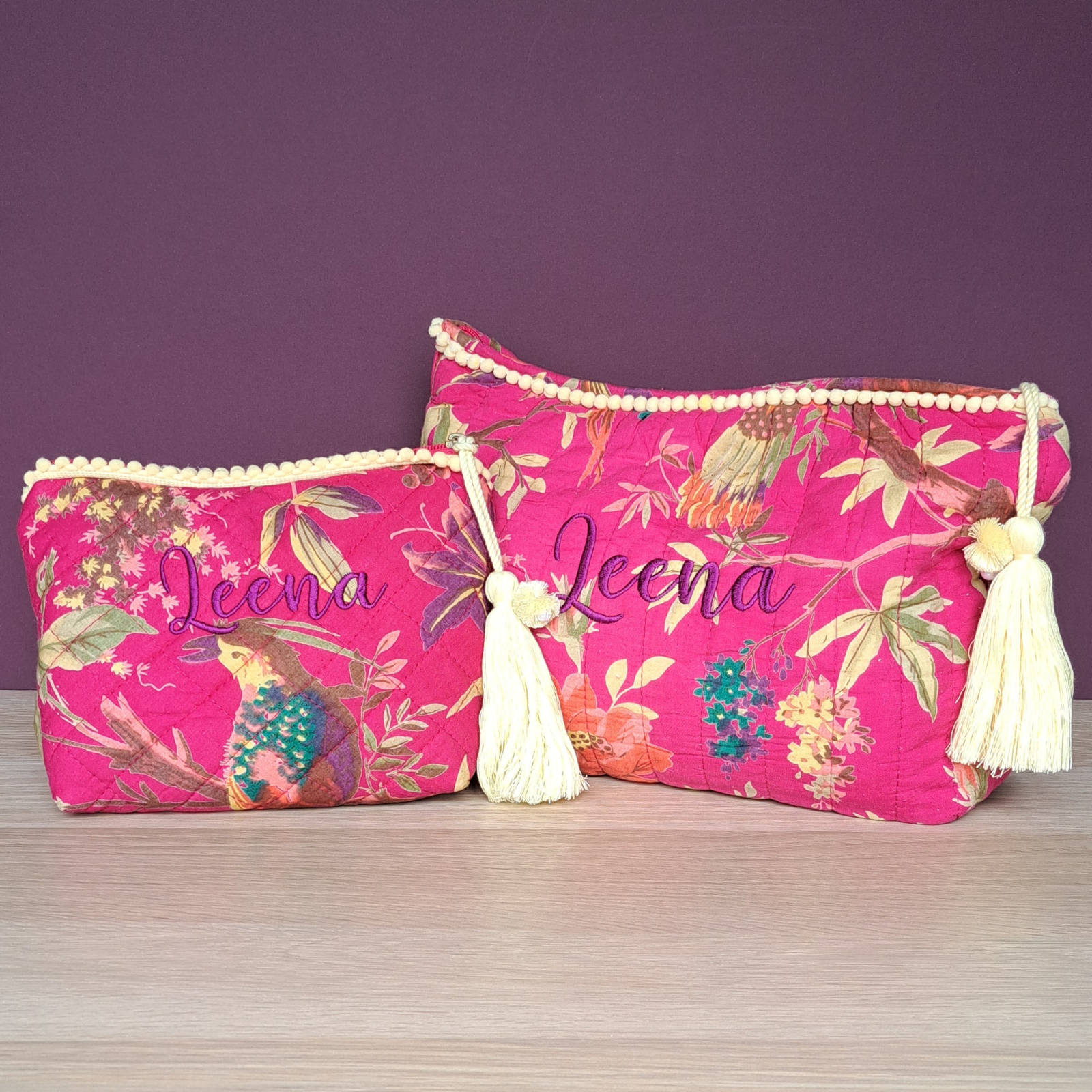 Image of a personalised make up bag and matching toiletries bag. The bags are made from quilted cotton with a vibrant pink design with exotic birds and flowers. The bags are lined with white water resistant fabric and have a lemon coloured tassle on the zip pull as well as lemon pom pom decorations along the top of each bag.