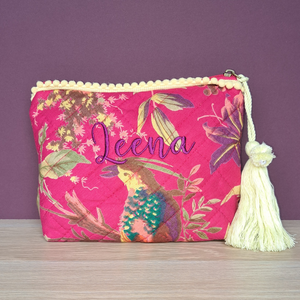 Image of a personalised make up bag. The bag is made from quilted cotton with a vibrant pink design with exotic birds and flowers. The bag is lined with white water resistant fabric and has a lemon coloured tassle on the zip pull as well as lemon pom pom decorations along the top.