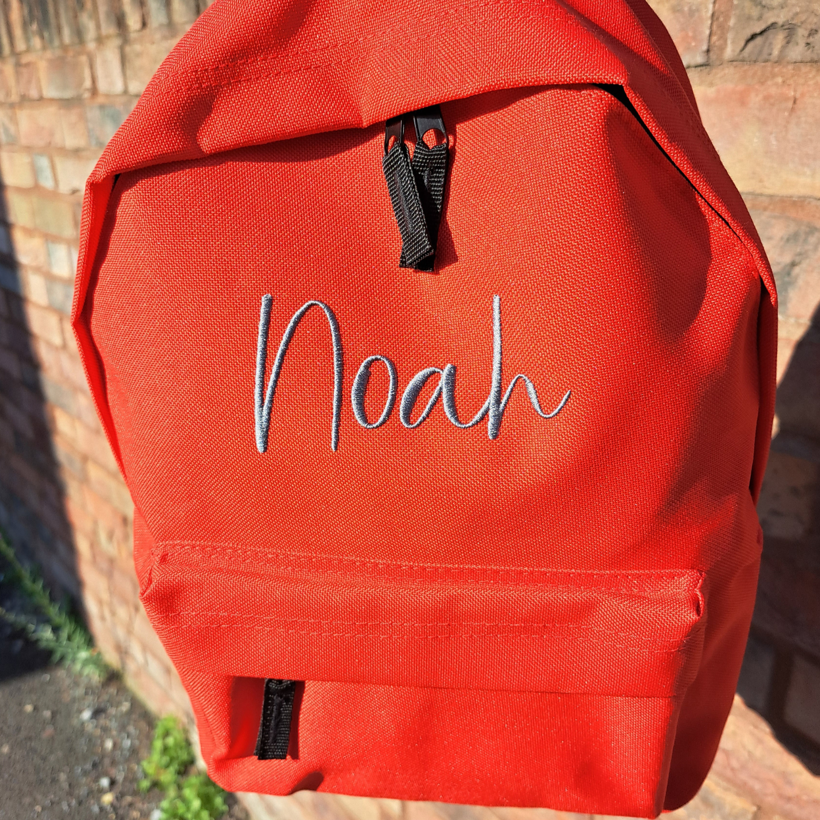 Image of a personalised rucksack for nursery or school which has been personalised with the name Noah in a grey slate embroidery thread. The bag has a main zipped compartment as well as a zipped smaller pocket on the front and two adjustable back straps.