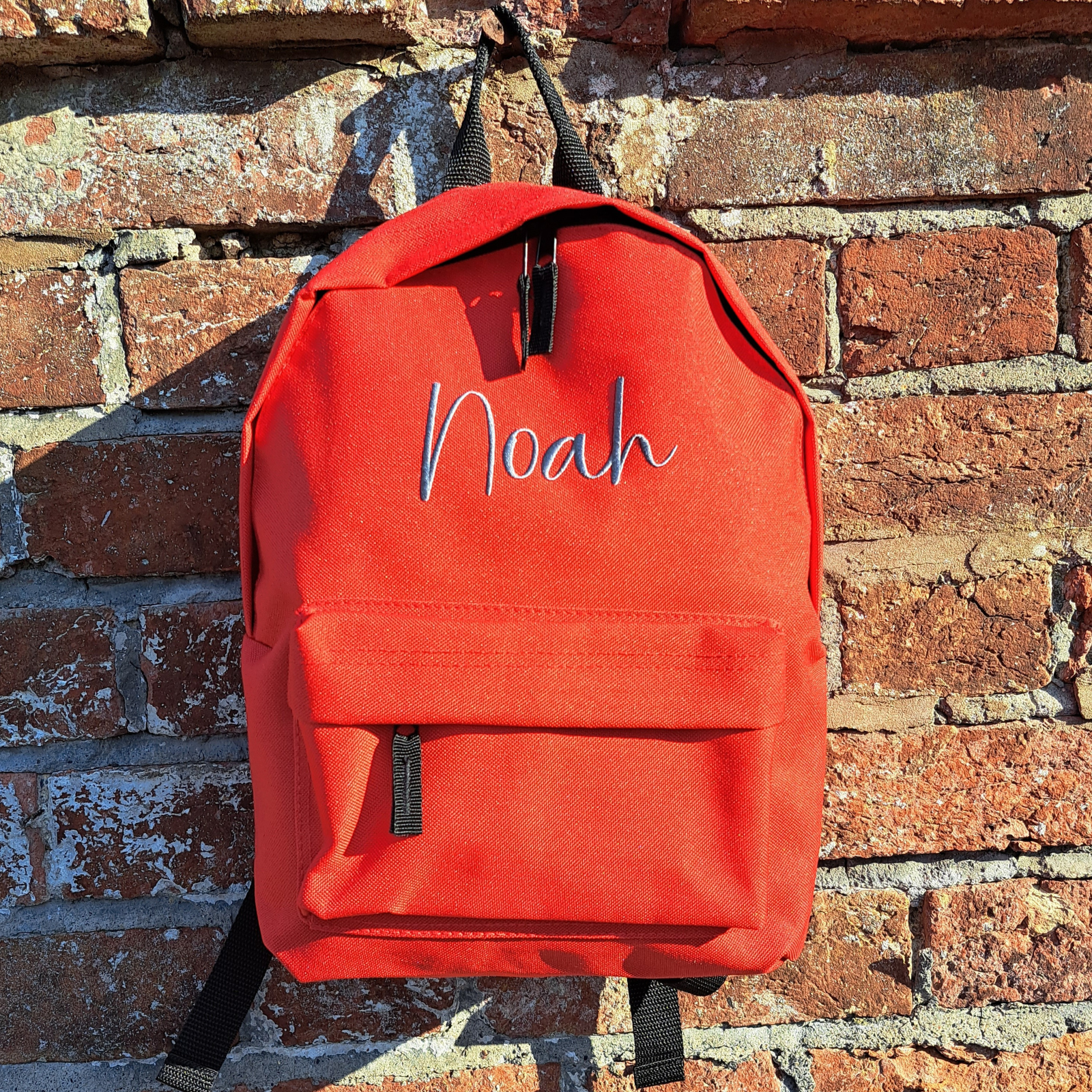 Image of a personalised rucksack for nursery or school which has been personalised with the name Noah in a grey slate embroidery thread. The bag has a main zipped compartment as well as a zipped smaller pocket on the front and two adjustable back straps.