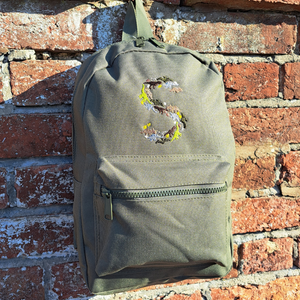 Image of a khaki green child's rucksack which has been embroidered on the front with a capital S which is made up from images of dinosaurs, footprints and eggs, in different coloured threads which compliment the colour of the bag. The bag is available in pistachio, powder pink, powder blue, light grey, fuchsia pink, navy blue, black, lavender and olive green.