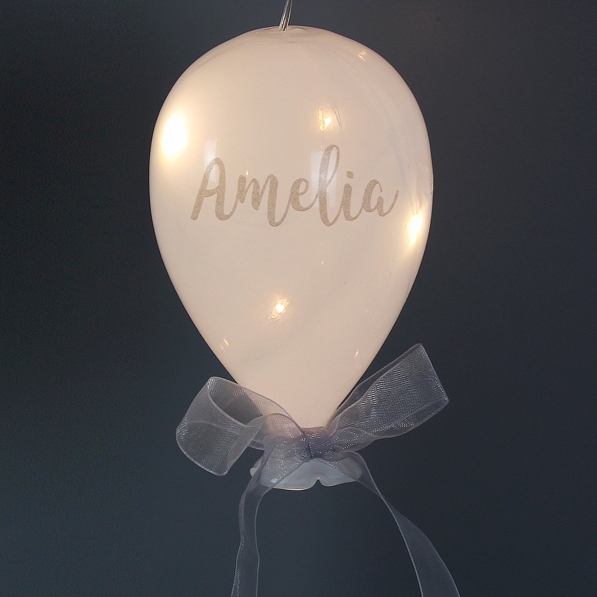 Personalised opaque white glass balloon decoration with battery powered LED lights inside. The balloon can be personalised with a name in a silver hand-written modern font and there is a silver ribbon tied into a bow at the bottom of the balloon.