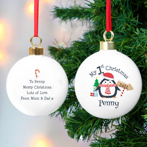 Image of the front and back of a personalised Christmas bauble. The bauble is white, the front features an image of a penguin with a hat on and scarf on. There is a small tree and gifts next to the penguin and an arrow sign with a year. Above the penguin in black text is ‘My 1st Christmas’ and below the penguin you can add a name. The back of the bauble has a small red and white candy cane and below it you can add your own message which will be printed in a black font.