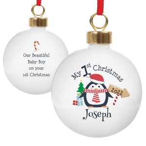 Image of the front and back of a personalised Christmas bauble. The bauble is white, the front features an image of a penguin with a hat on and scarf on. There is a small tree and gifts next to the penguin and an arrow sign with a year. Above the penguin in black text is ‘My 1st Christmas’ and below the penguin you can add a name. The back of the bauble has a small red and white candy cane and below it you can add your own message which will be printed in a black font.