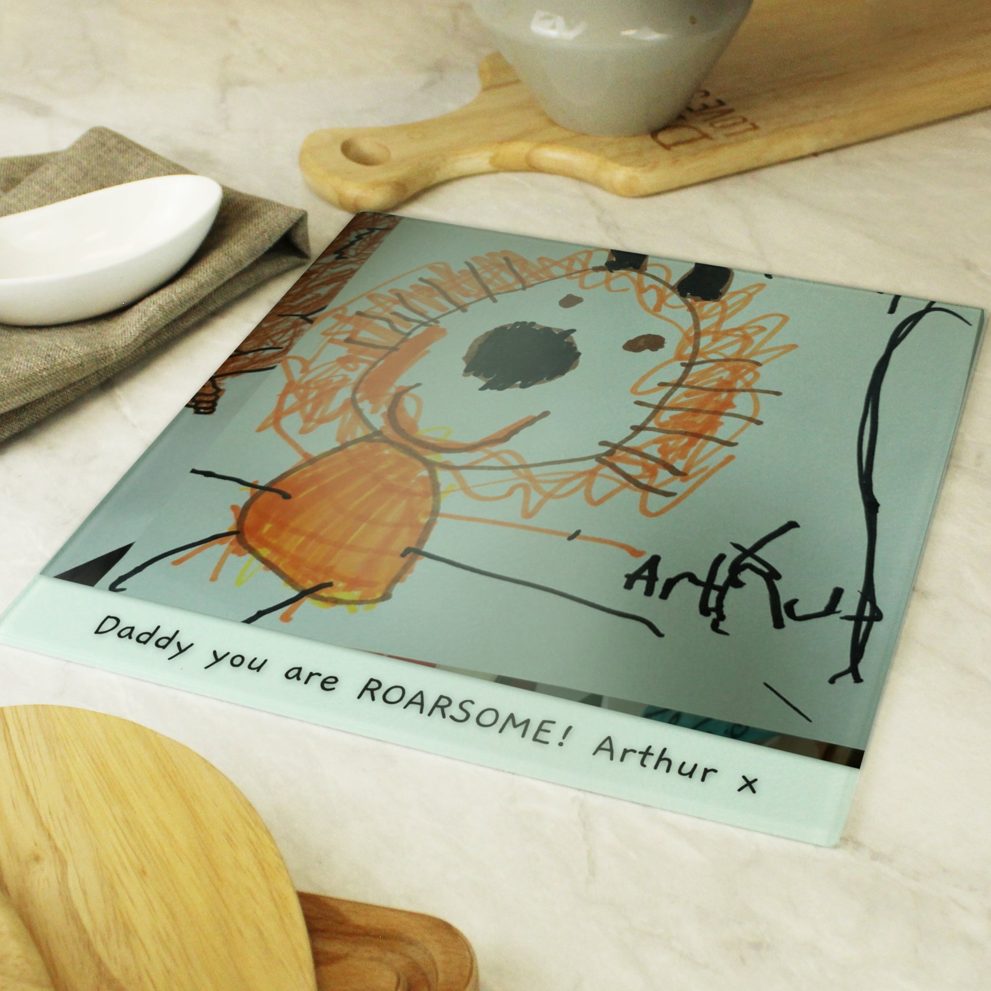 Image of a glass chopping board that can be personalised by having your child's own drawing printed on it and underneath the drawing, you can choose to add your own message or text which will be printed in a black handwritten style font.