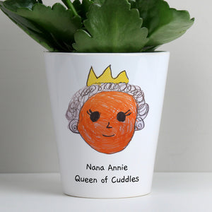 Image of a white ceramic plant pot with a plant inside it. The plant pot can be printed with your child's own artwork that will be printed on the front and there is space underneath the artwork for you own optional text which will be printed in a black handwritten style font.