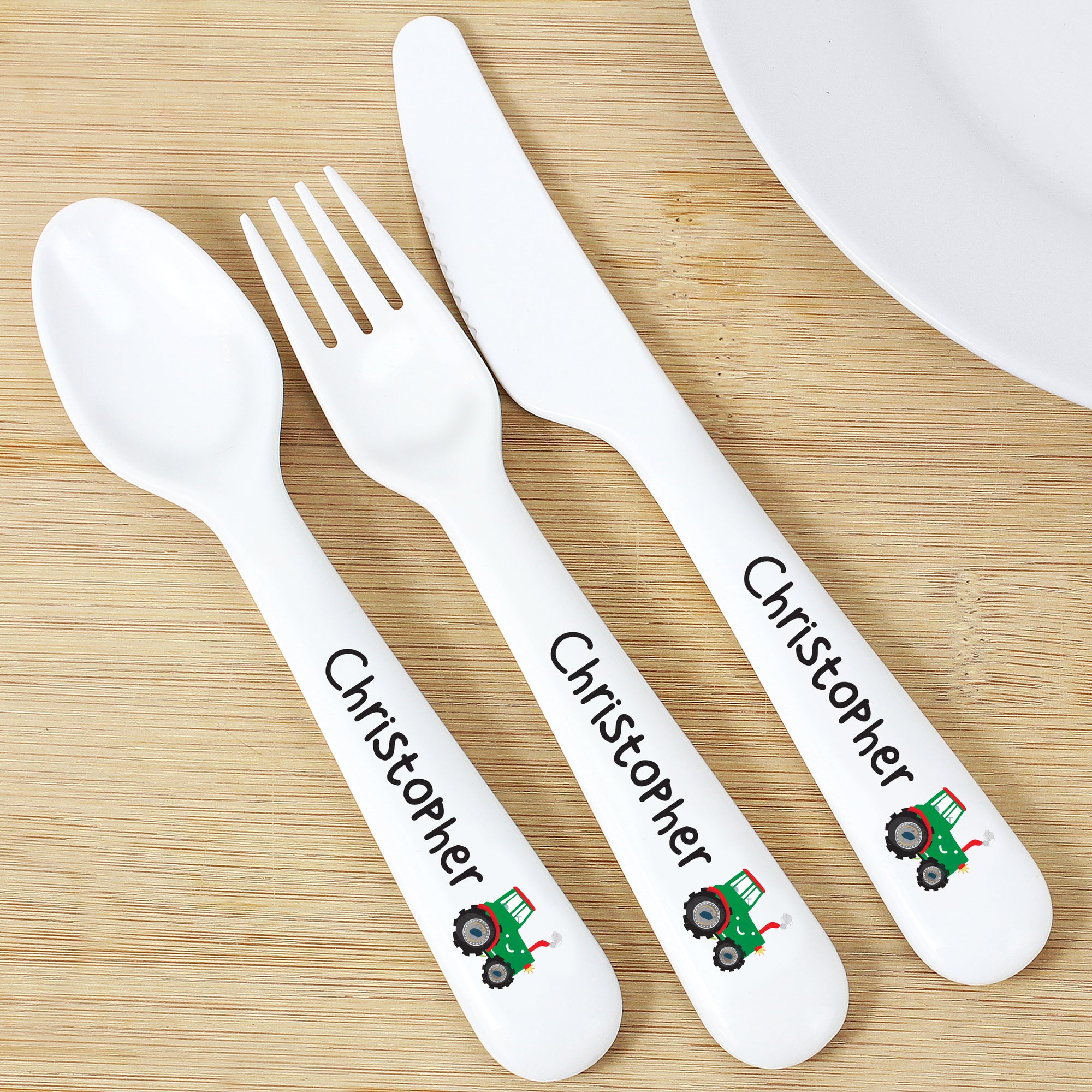 Image of a plastic BPA free child's cutlery set. The cutlery set comprises of a spoon, fork and knife that are white and there is an image of a green tractor at the end of the handle. The handles can also be personalised with a name of your choice of up to 12 characters which will be printed in black.