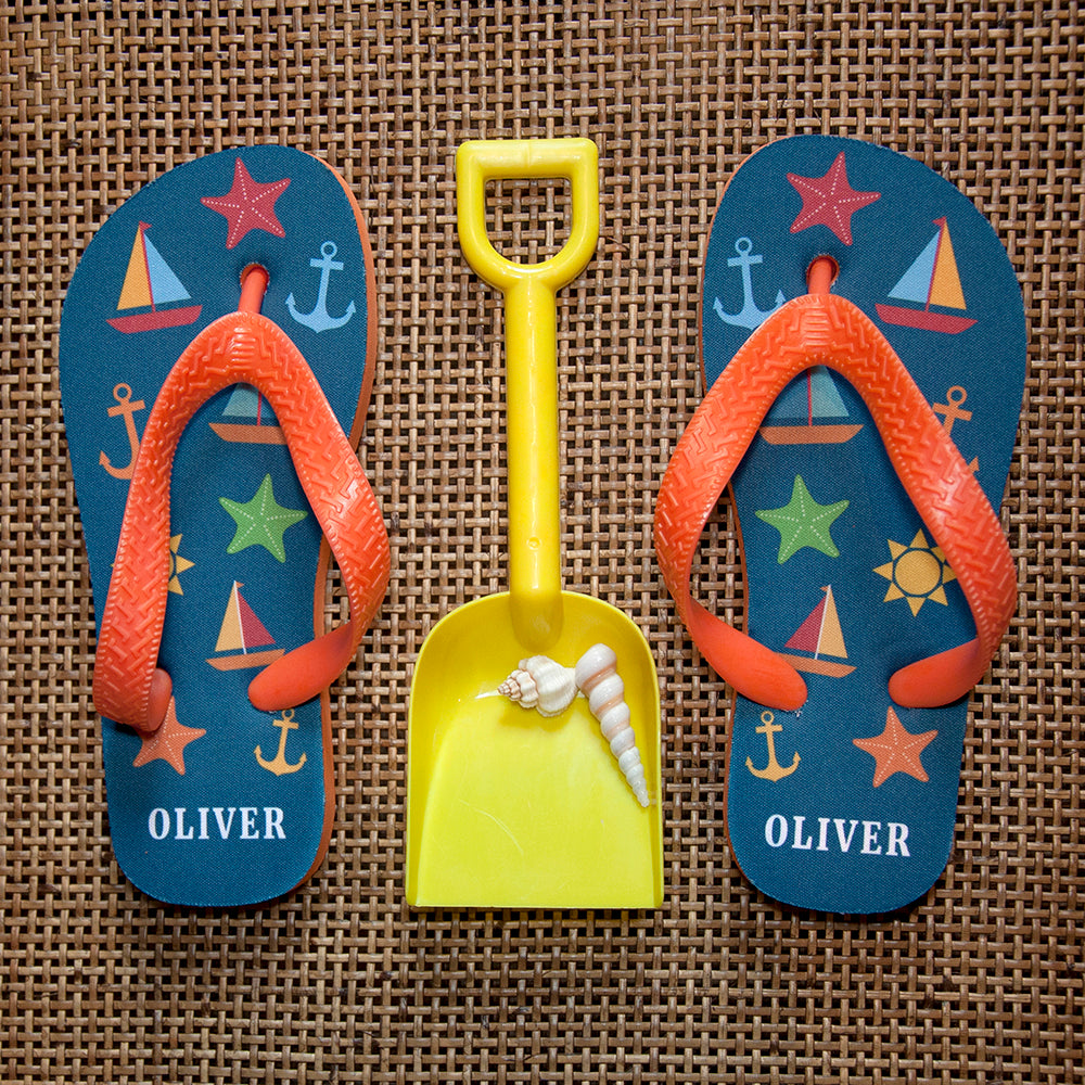 Image of a pair of children's personalised flip flops. The flip flops have an orange sole and straps, and the flip flops have illustrations of bright beach themed items such as sail boats, star fish, anchors and a sun on a blue background. The flip flops can be personalised wtih a name of up to 10 characters on the heel. The flip flops are available in 3 different child sizes.