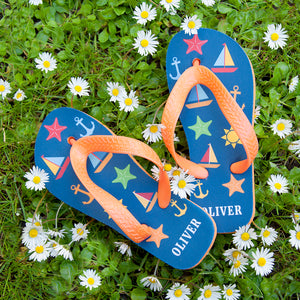 Image of a pair of child's personalised flip flops. The flip flops have an orange sole and straps, and the flip flops have illustrations of bright beach themed items such as sail boats, star fish, anchors and a sun on a blue background. The flip flops can be personalised wtih a name of up to 10 characters on the heel. The flip flops are available in 3 different chilld sizes.