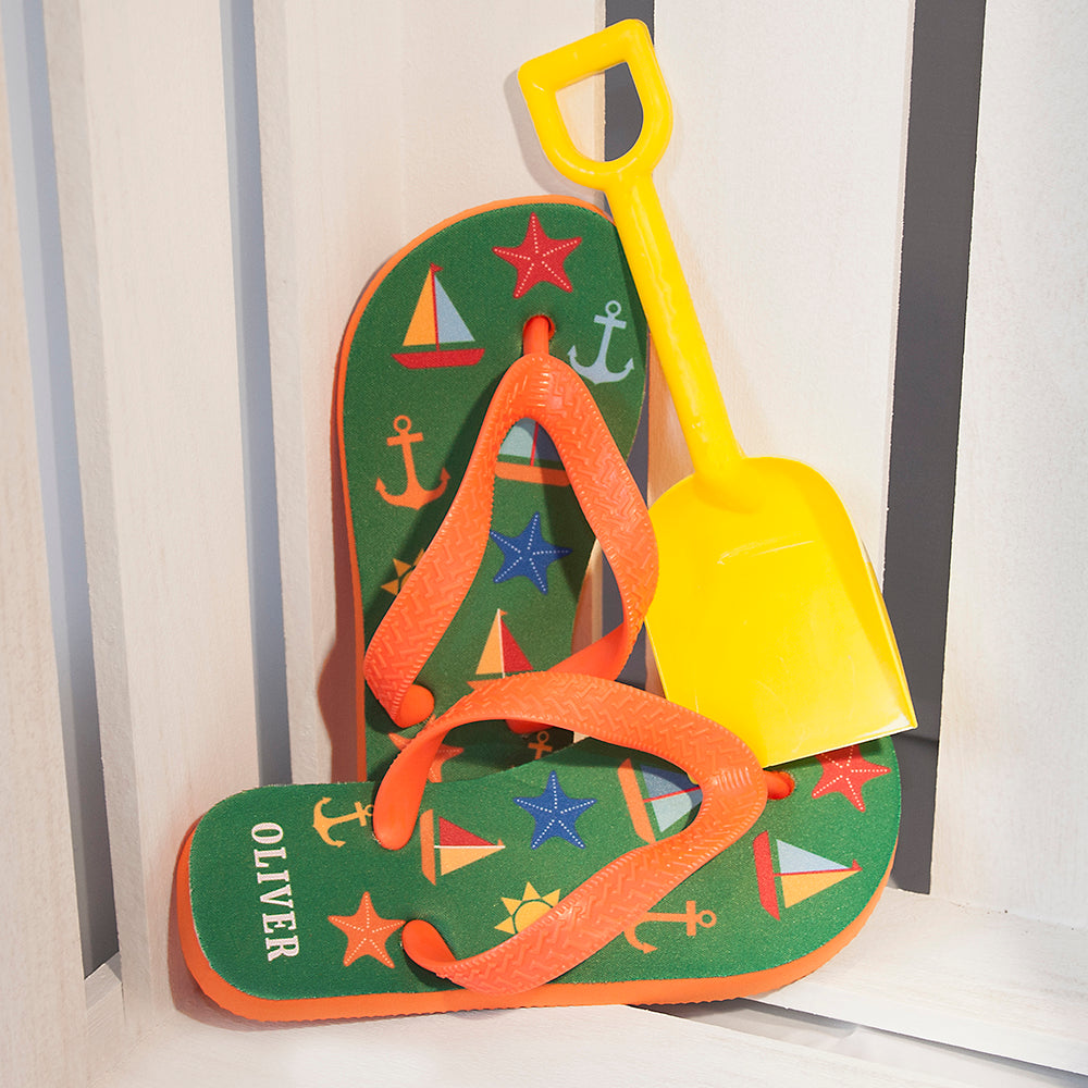 Image of a pair of children's personalised flip flops. The flip flops have an orange sole and straps, and the flip flops have illustrations of bright beach themed items such as sail boats, star fish, anchors and a sun on a green background. The flip flops can be personalised wtih a name of up to 10 characters on the heel. The flip flops are available in 3 different child sizes.