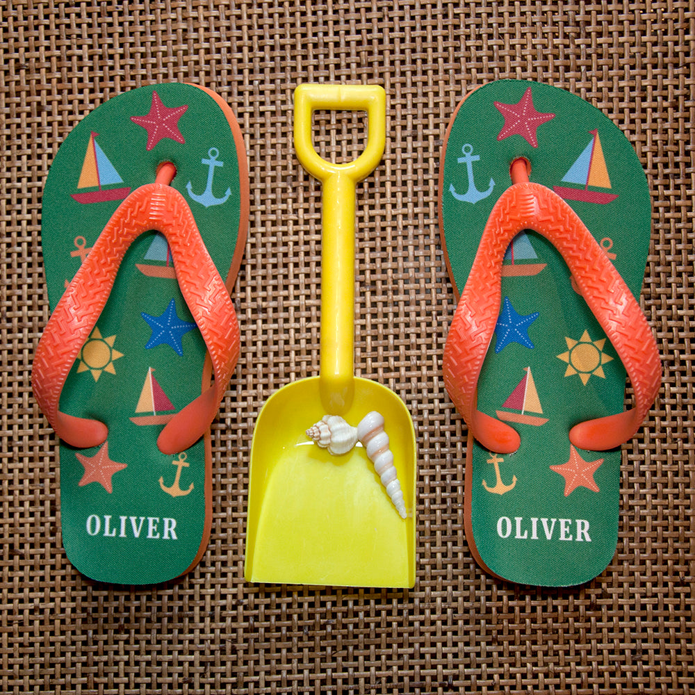 Image of a pair of children's personalised flip flops. The flip flops have an orange sole and straps, and the flip flops have illustrations of bright beach themed items such as sail boats, star fish, anchors and a sun on a green background. The flip flops can be personalised wtih a name of up to 10 characters on the heel. The flip flops are available in 3 different child sizes.