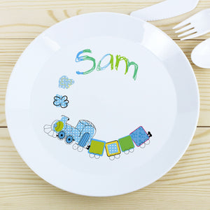 Image of a white plastic BPA free childs personalised plate. The plate is white with a rim and in the centre of the plate is a cartoon drawing of a blue and green train with smoke coming out of the train's funnel. The plate can be personalised with a name up to 12 characters which will be printed above the steam in a mixture of blue and green. The plate is part of a set and comes with a cutlery set in the same theme.