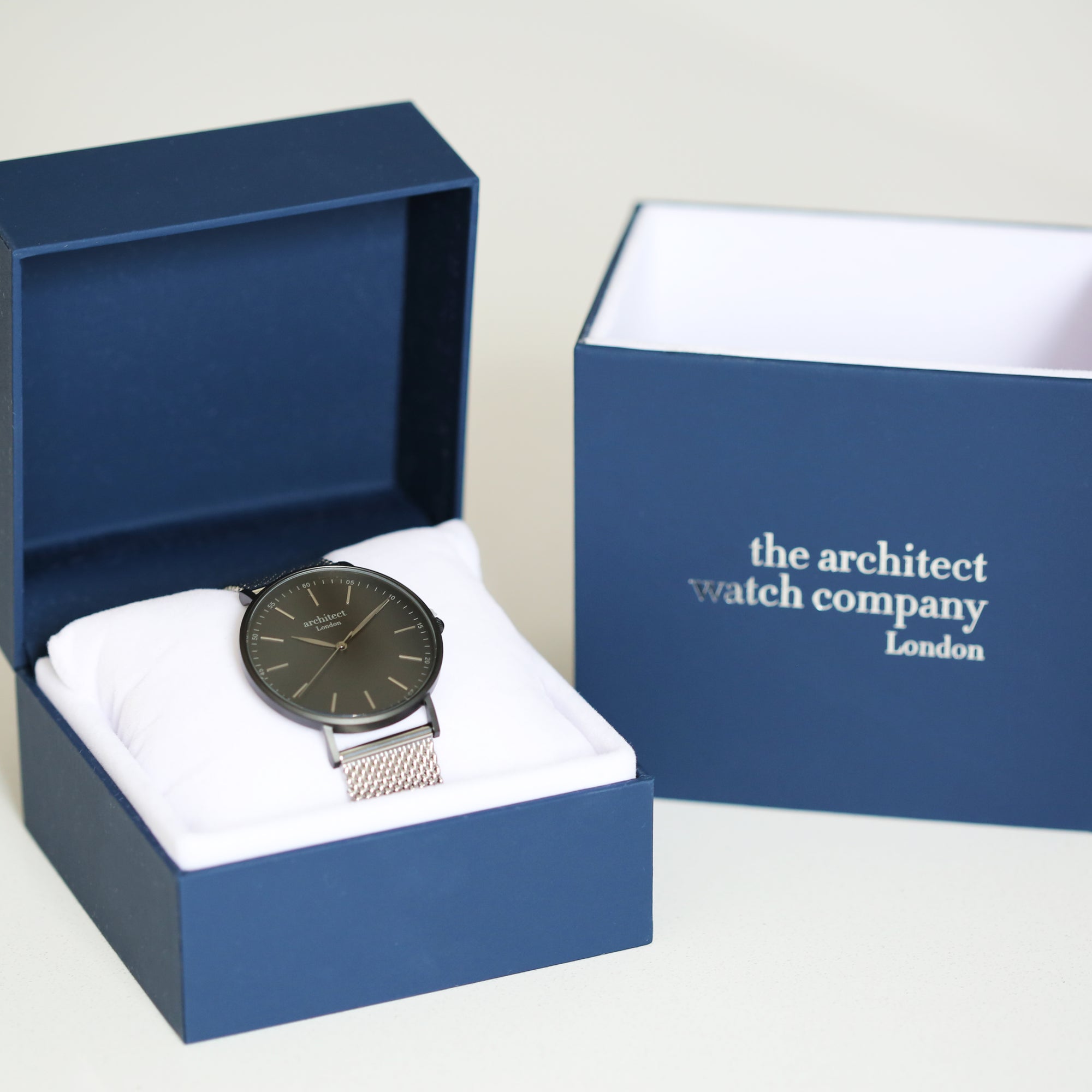 Image of a man's watch in a blue presentation box. The watch can be engraved on the back with your own handwriting. The watch is made by The Architect Watch Company London and has a large black face and a stainless steel mesh strap. The rear of the watch can be engraved with your message written in your own handwriting.