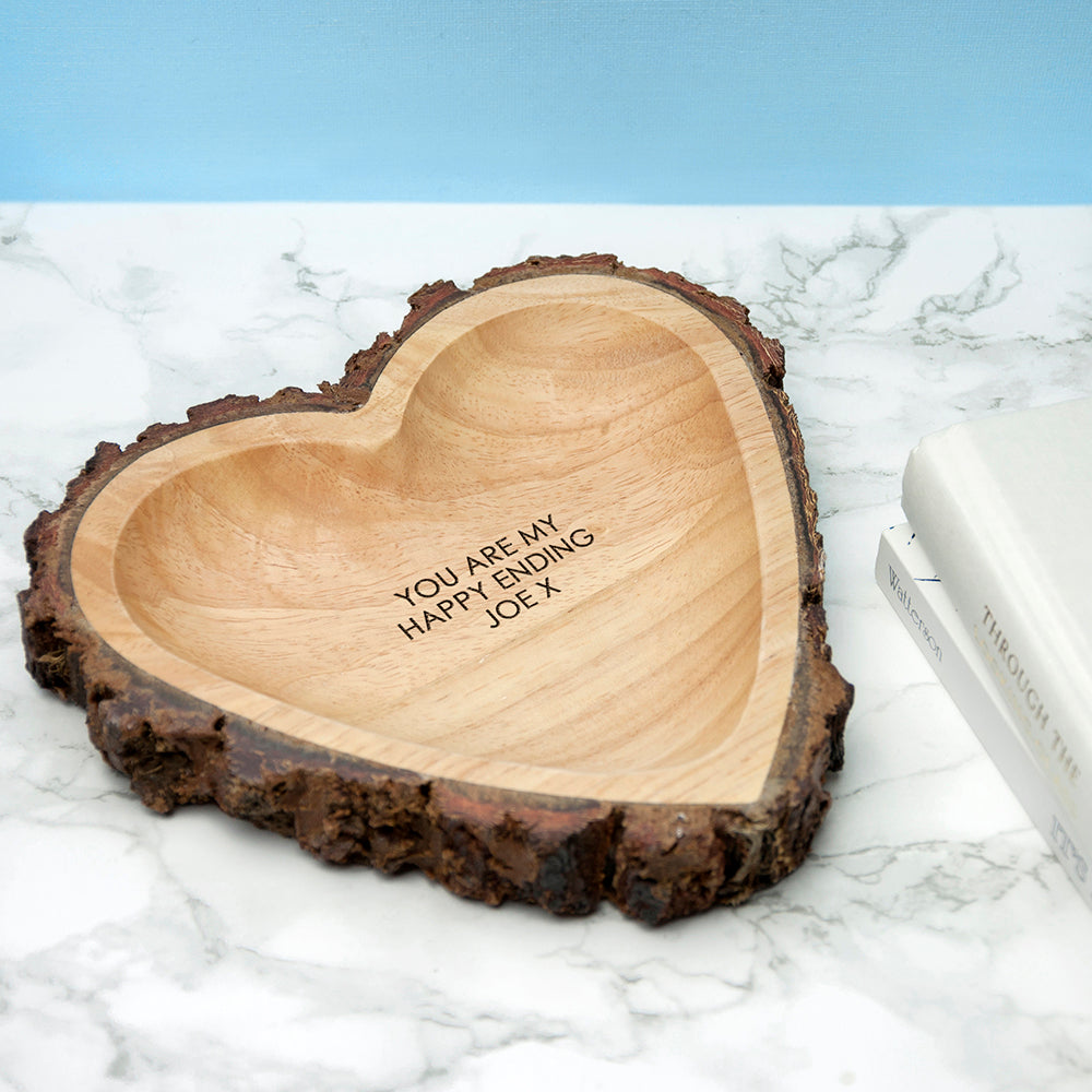 Image of a hand-carved heart-shaped wooden bowl that has a rustic natural bark edging. The bowl can be personalised with your own message which will be engraved in an upper case font.