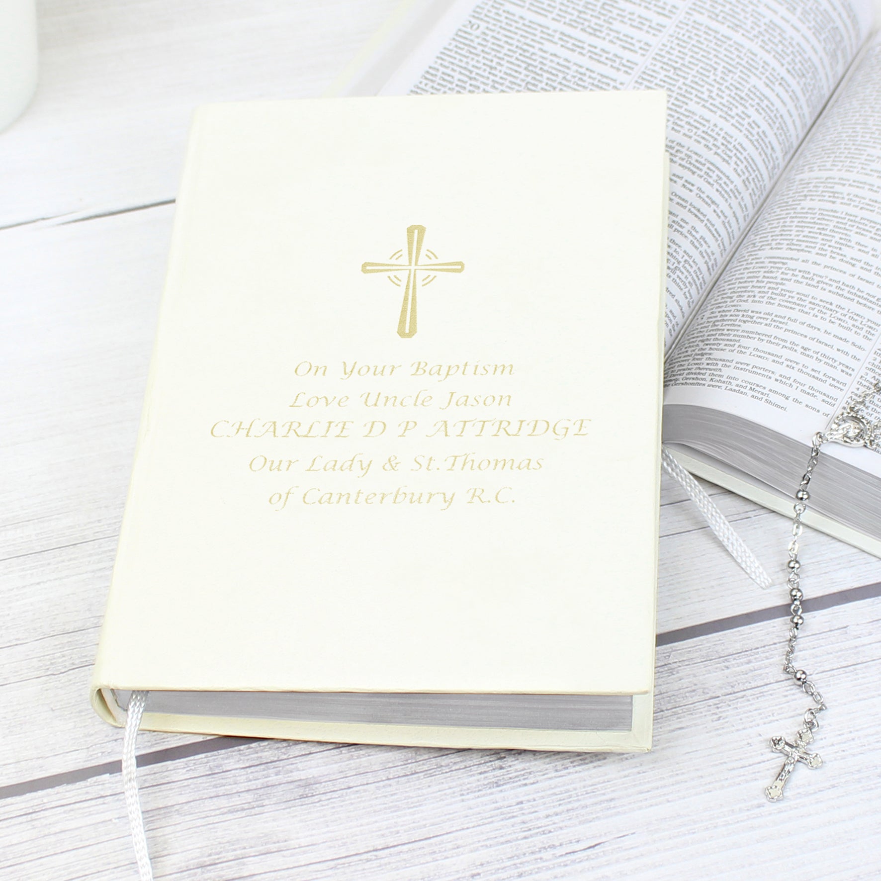 Image of a bible with white cover that can be personalised with 5 lines of your own text. A cross is printed above the text, all of which is printed in gold. The bible has a ribbon bookmark and the pages are made from 100% recycled paper.