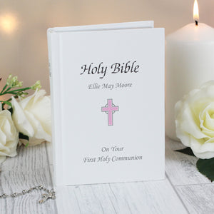 Image of a holy bible with a white leatherette cover featuring the text 'Holy Bible' and a pink cross. The cover can be personalised with 3 lines of text, one line will appear above the image of the cross and the remaining two lines will appear below the image of the cross. The text is printed in silver and the bible has a ribbon bookmark and the pages are edged in silver leaf.