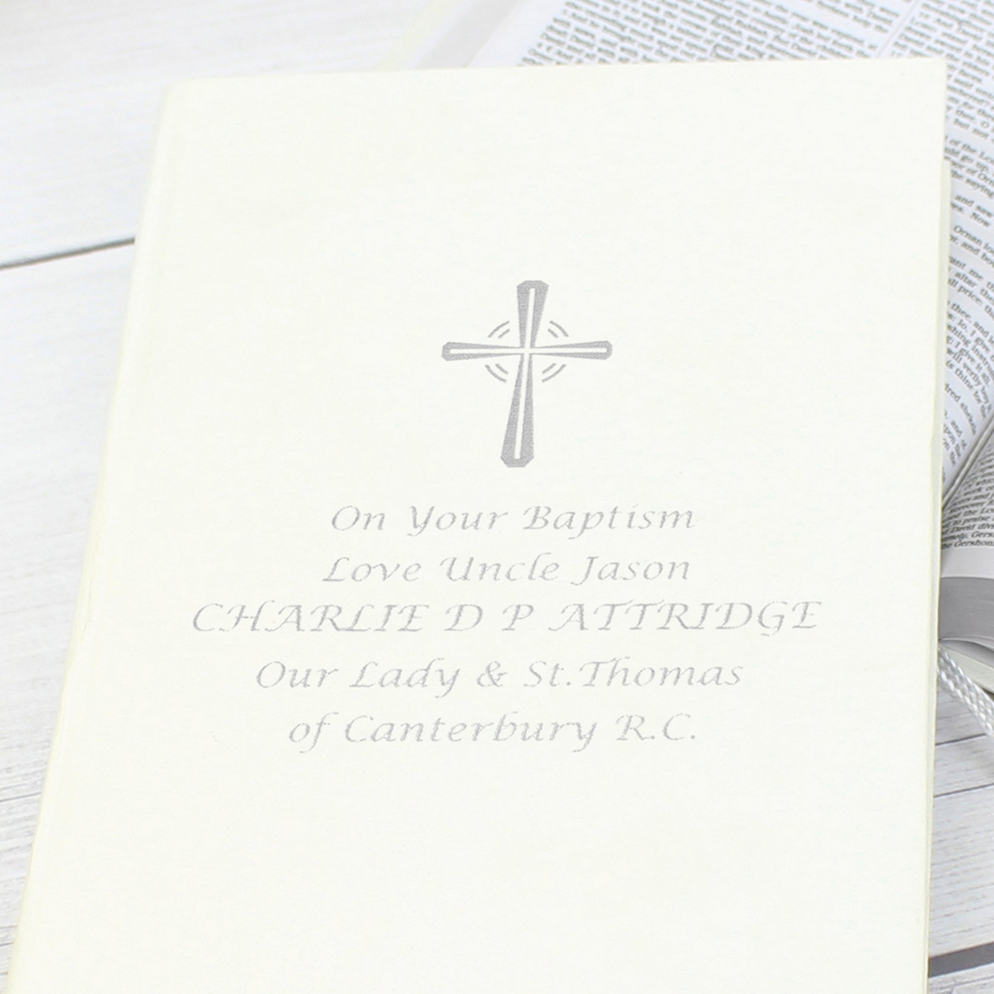 Image of a bible with white cover that can be personalised with 5 lines of your own text. A cross is printed above the text, all of which is printed in silver. The bible has a ribbon bookmark and the pages are made from 100% recycled paper.