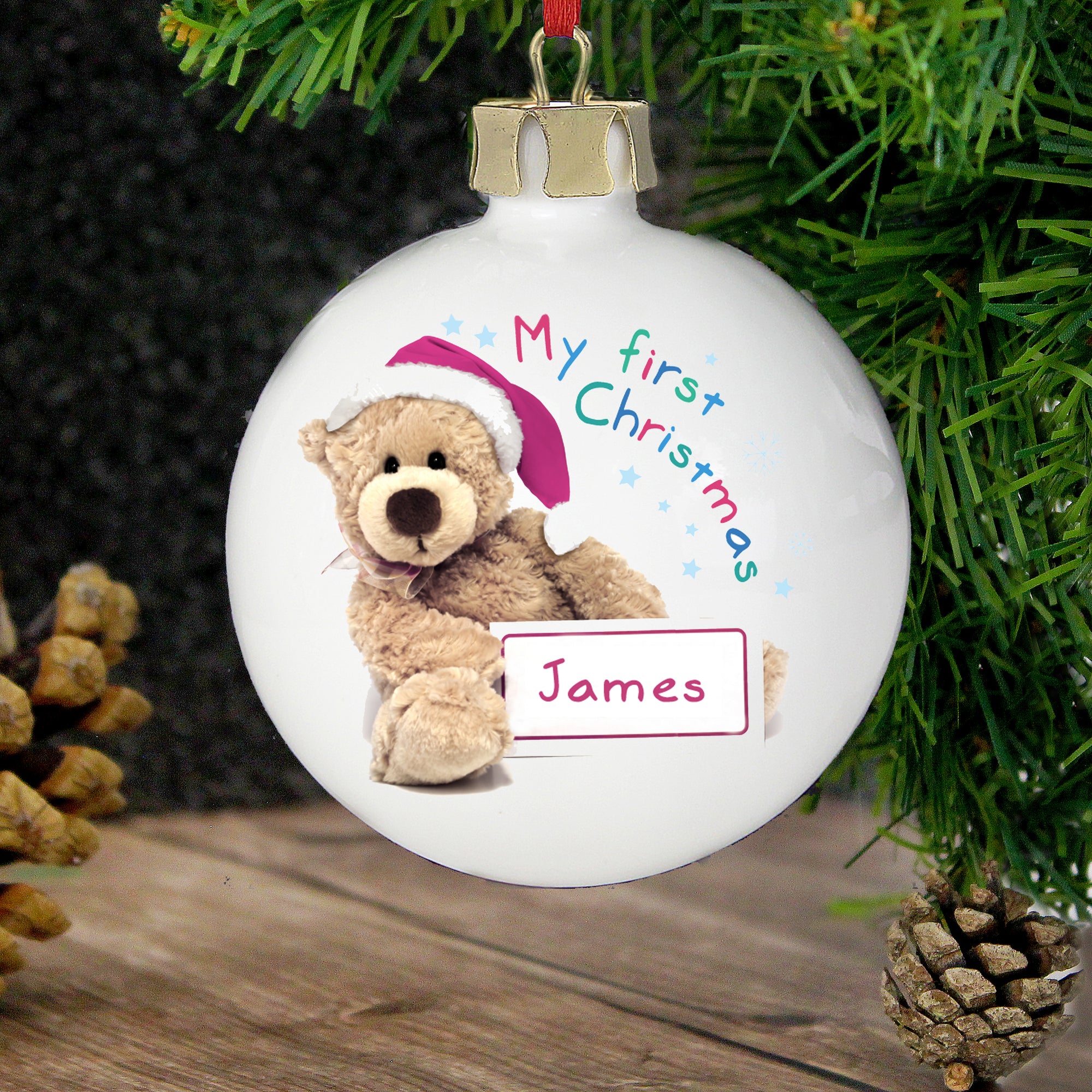 Personalised Christmas decoration featuring the text 'My first Christmas' in bright lettering and underneath that, a cute teddy bear wearing a red Christmas hat on the front, holding a sign that can be personalised with a name of your choice. The rear of the bauble can be personalised with your own special message over up to 4 lines.