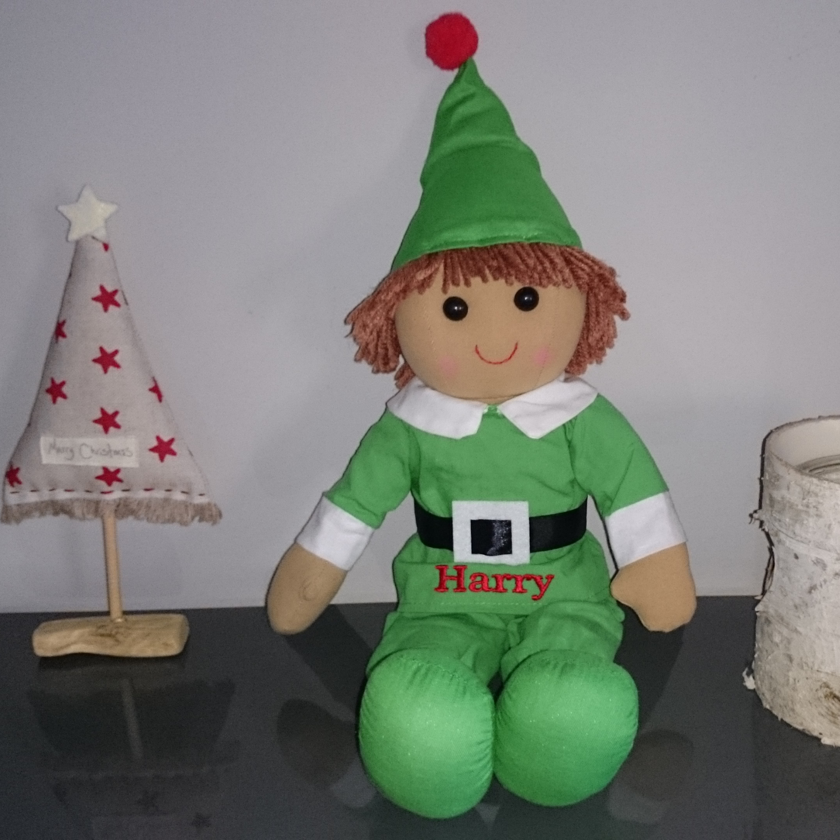 Personalised friendly Christmas elf soft toy wearing a green suit and green pointed hat with a red bauble. The green suit on the elf can be personalised with a name of your choice. The elf measures approximately 40 cm tall.