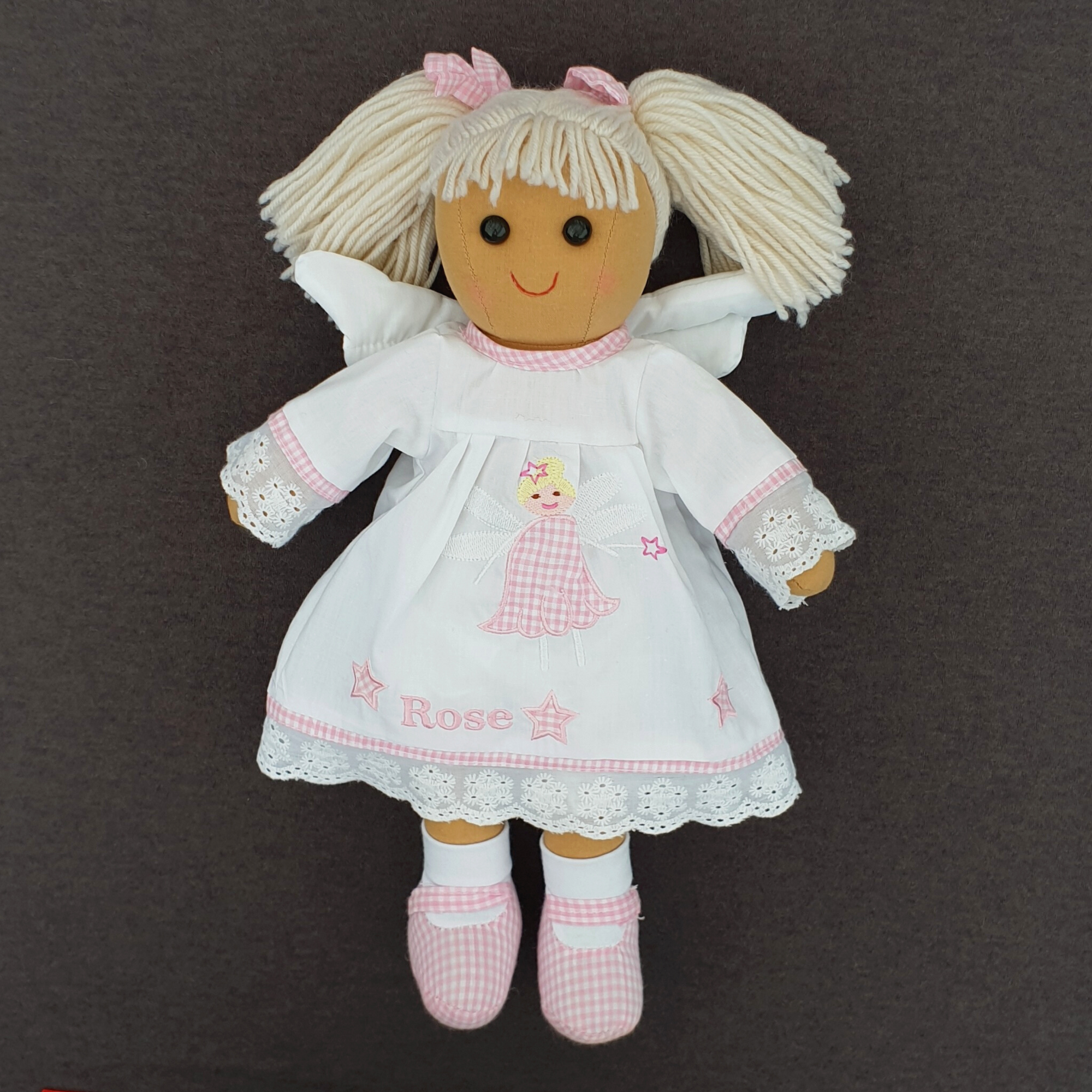 Personalised fairy ragdoll. This ragdoll has blonde hair tied in two bunches and is wearing a white dress with pink gingham decoration and she has fairy wings on her back. The dress can be personalised with a name of your choice of up to 6 characters.
