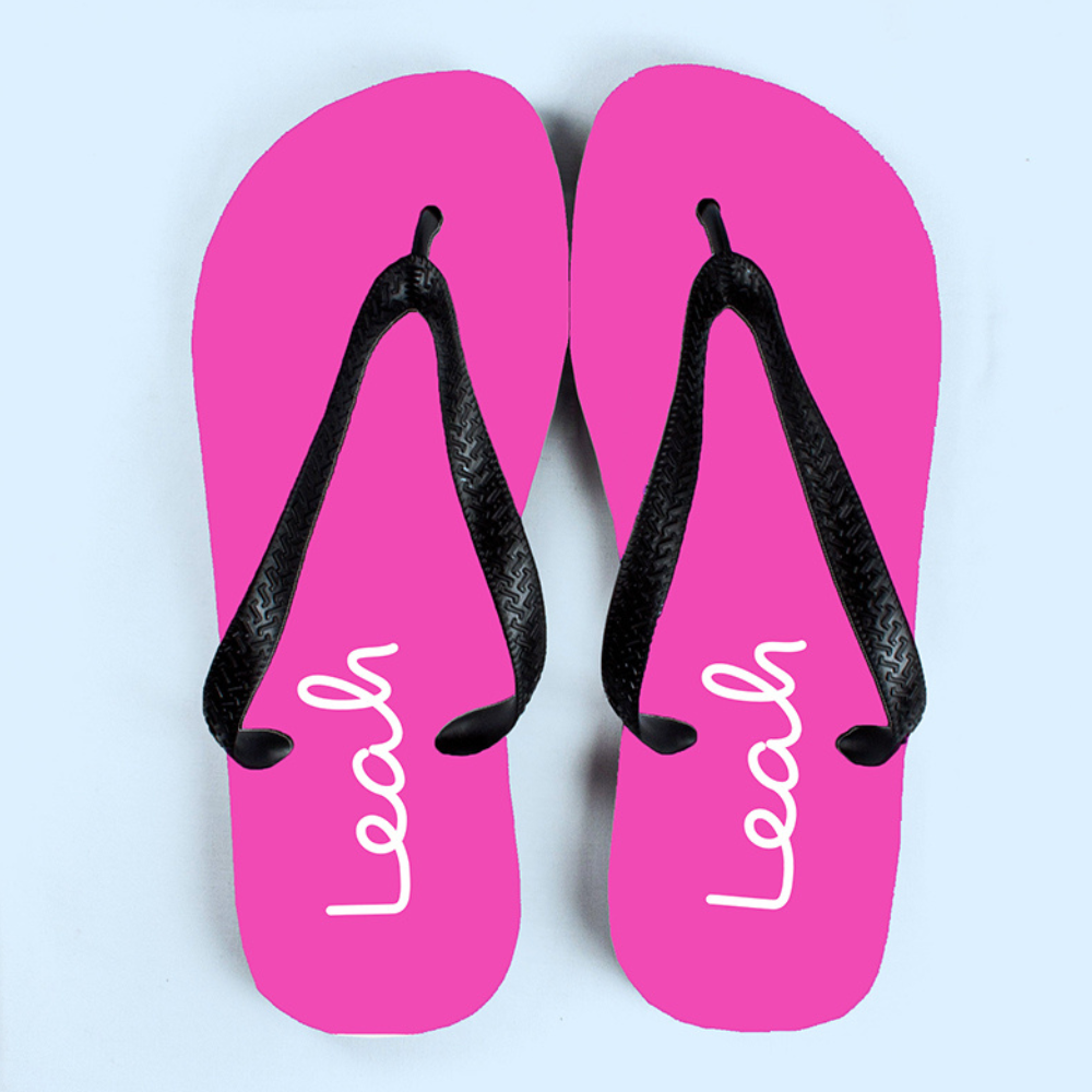 Image of a pair of pink flip flops that have been personalised with a name of your choice of up to 12 characters which will be printed in white. The flip flops have a black strap.