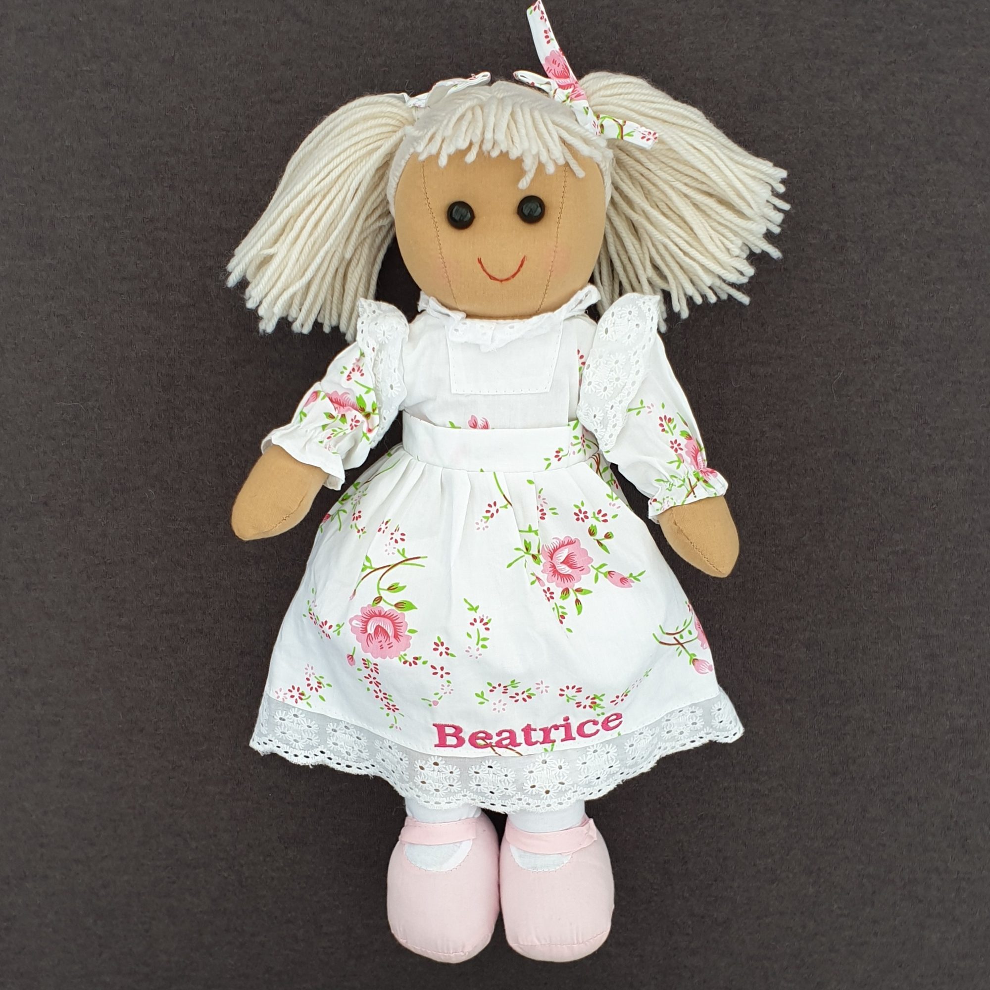 Personalised rag doll with blonde hair and a beautiful white dress with pink flowers on it. The dress can be personalised with a name of your choice.