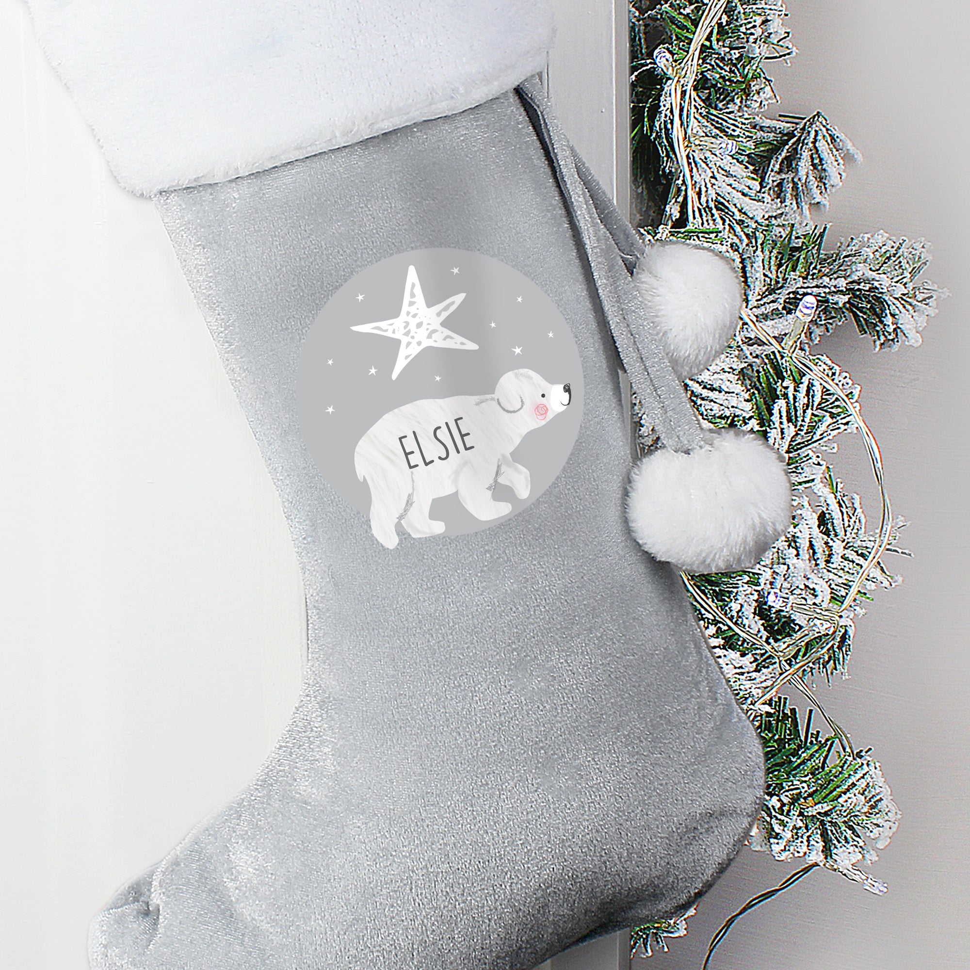 Personalised grey velvet Christmas stocking with a plush white trim. The front of the stocking features an illustration of a hand-drawn baby polar bear with a star above it and the stocking can be personalised with a name of your choice which will be printed in a black modern uppercase font inside the image of the bear.