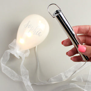 Personalised opaque white glass balloon decoration with battery powered LED lights inside. The balloon can be personalised with a name in a silver hand-written modern font and there is a silver ribbon tied into a bow at the bottom of the balloon.