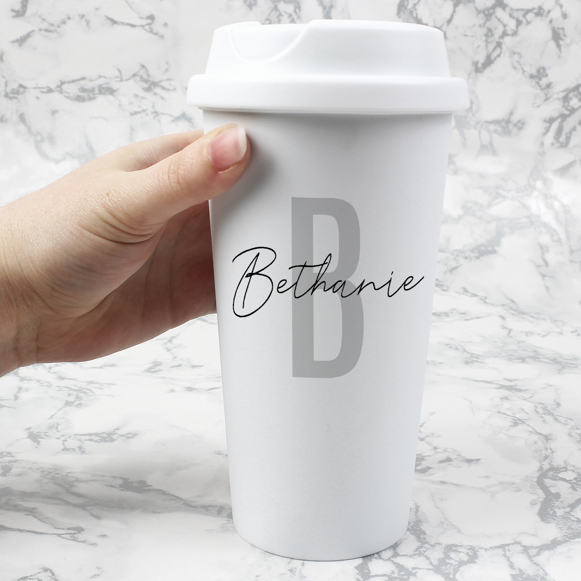 Image of a white plastic insulated travel mug with a screw top lid to help prevent spills. The cup can be personalised with an initial which will be printed in a large capital letter in grey and the full name will be printed over the initial in a place handwriting font.