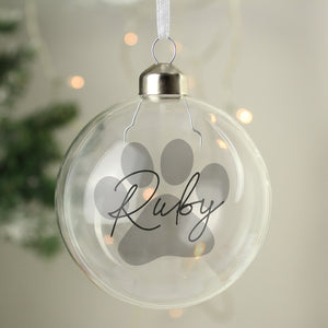 Image of a glass Christmas bauble for a pet with a large paw print design in grey. The bauble can be personalised with a name of your choice which will be printed in a black handwriting font across the paw print.
