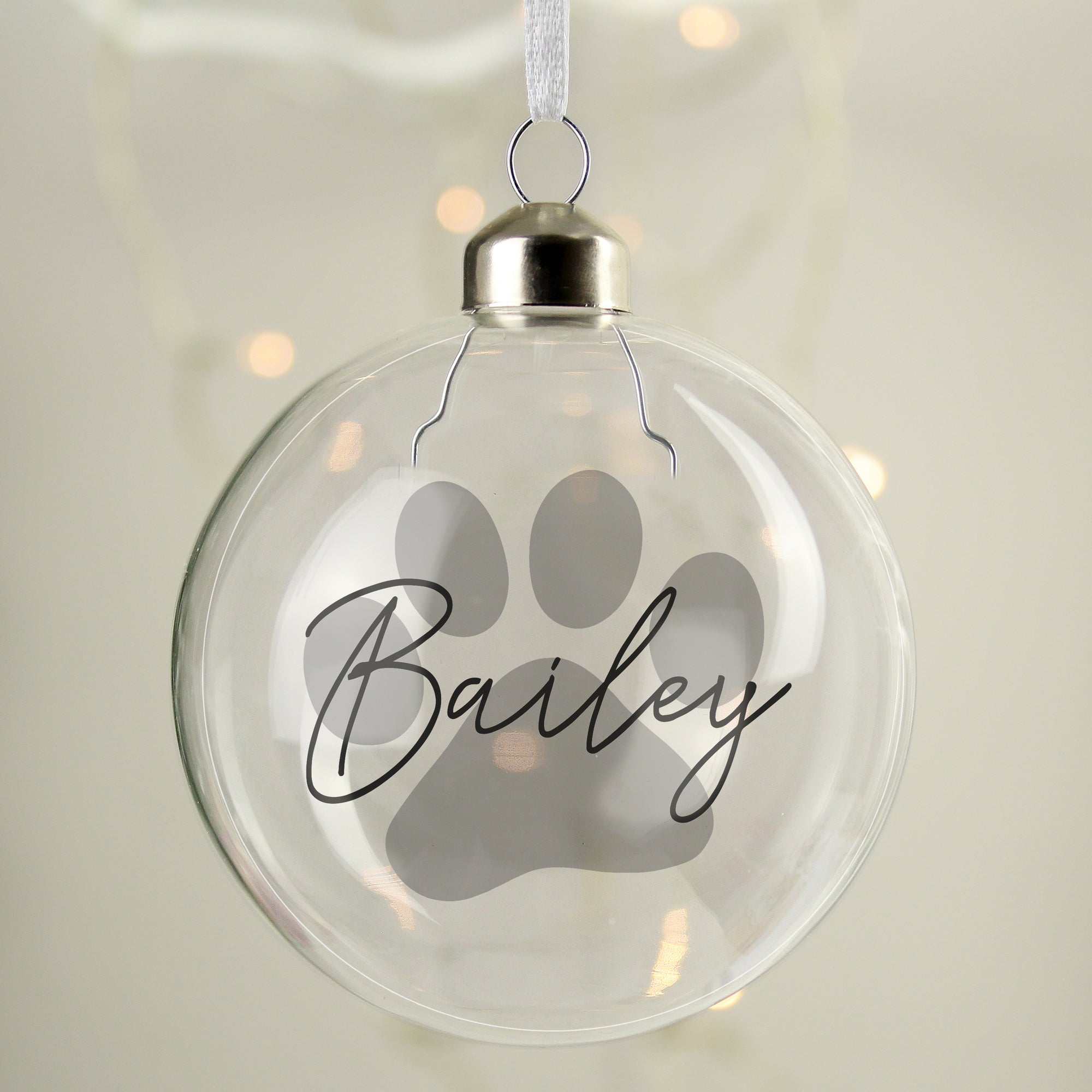 Image of a glass Christmas bauble for a pet with a large paw print design in grey. The bauble can be personalised with a name of your choice which will be printed in a black handwriting font across the paw print.