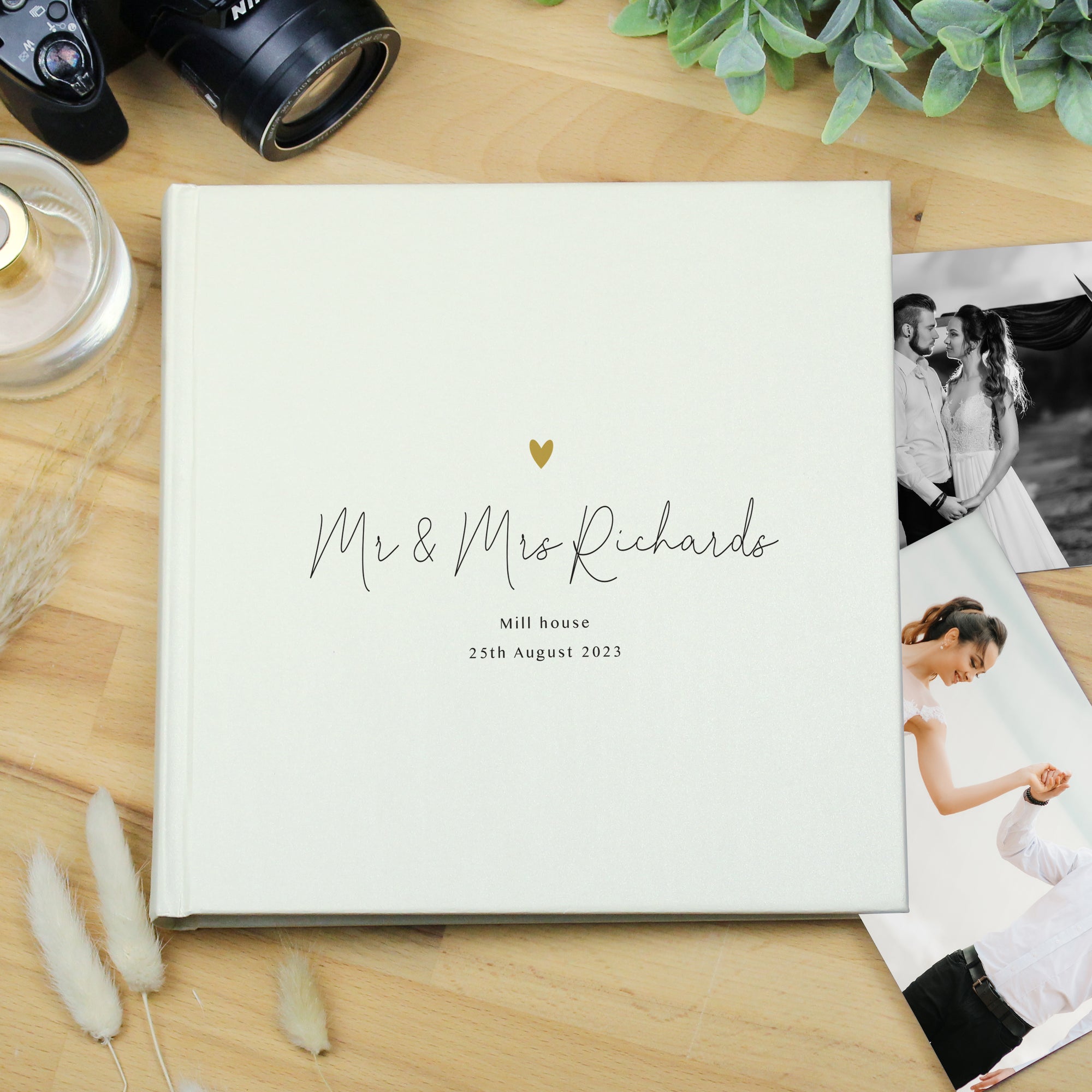 Image of a white square photo album that can hold up to 120 6" by 4" photos. The cover of the album features a small golden heart and beneath it you can add your own text over 3 lines. The text on the first line will appear in a large script font.