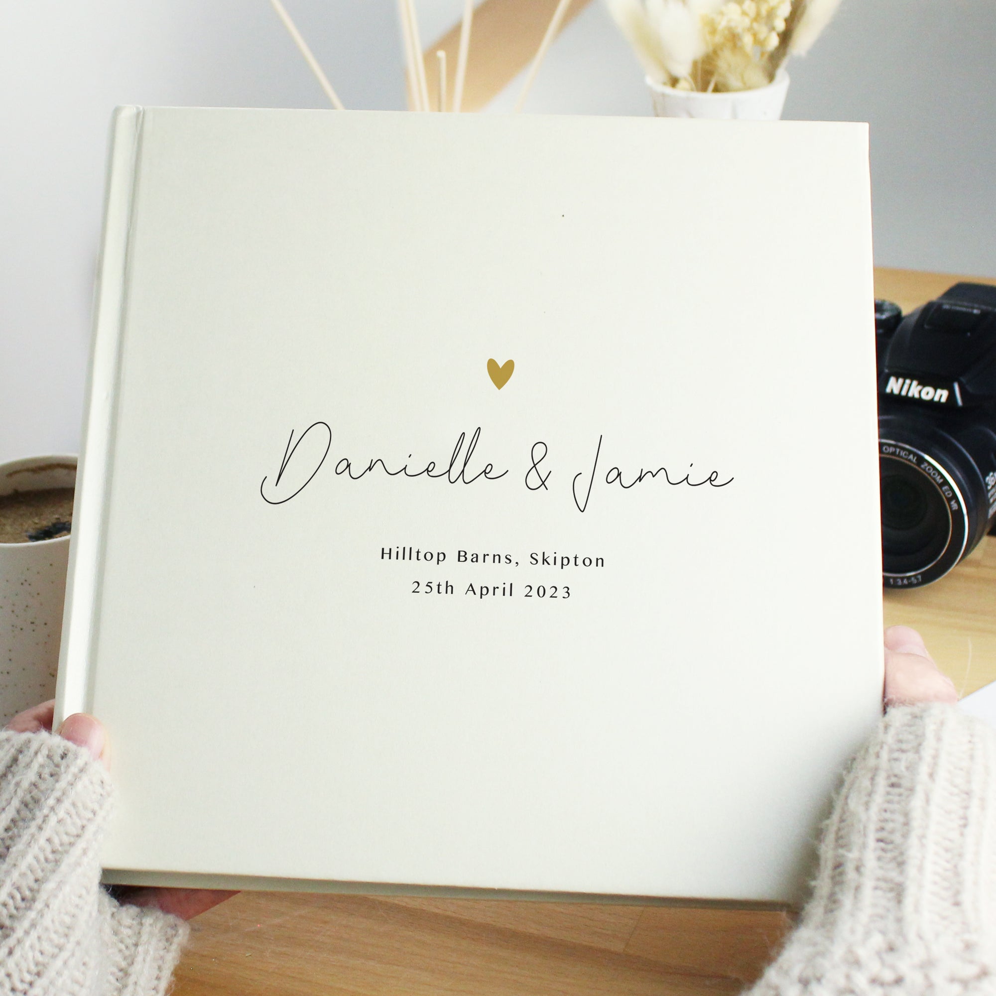 Image of a white square photo album that can hold up to 120 6" by 4" photos. The cover of the album features a small golden heart and beneath it you can add your own text over 3 lines. The text on the first line will appear in a large script font.