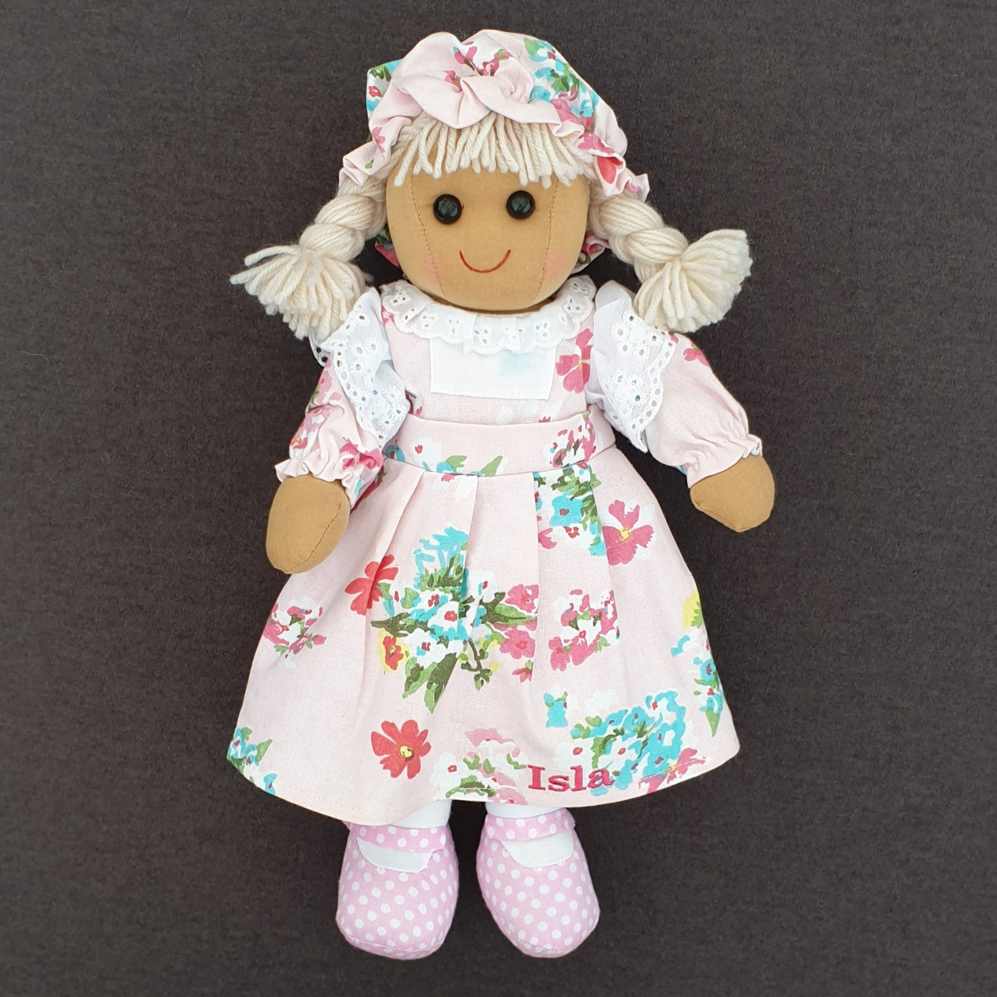 Personalised rag doll wearing a pink floral dress that can be personalised with a name of up to 10 characters plus a matching hat.  Underneath her dress she is wearing white pantaloons. 
