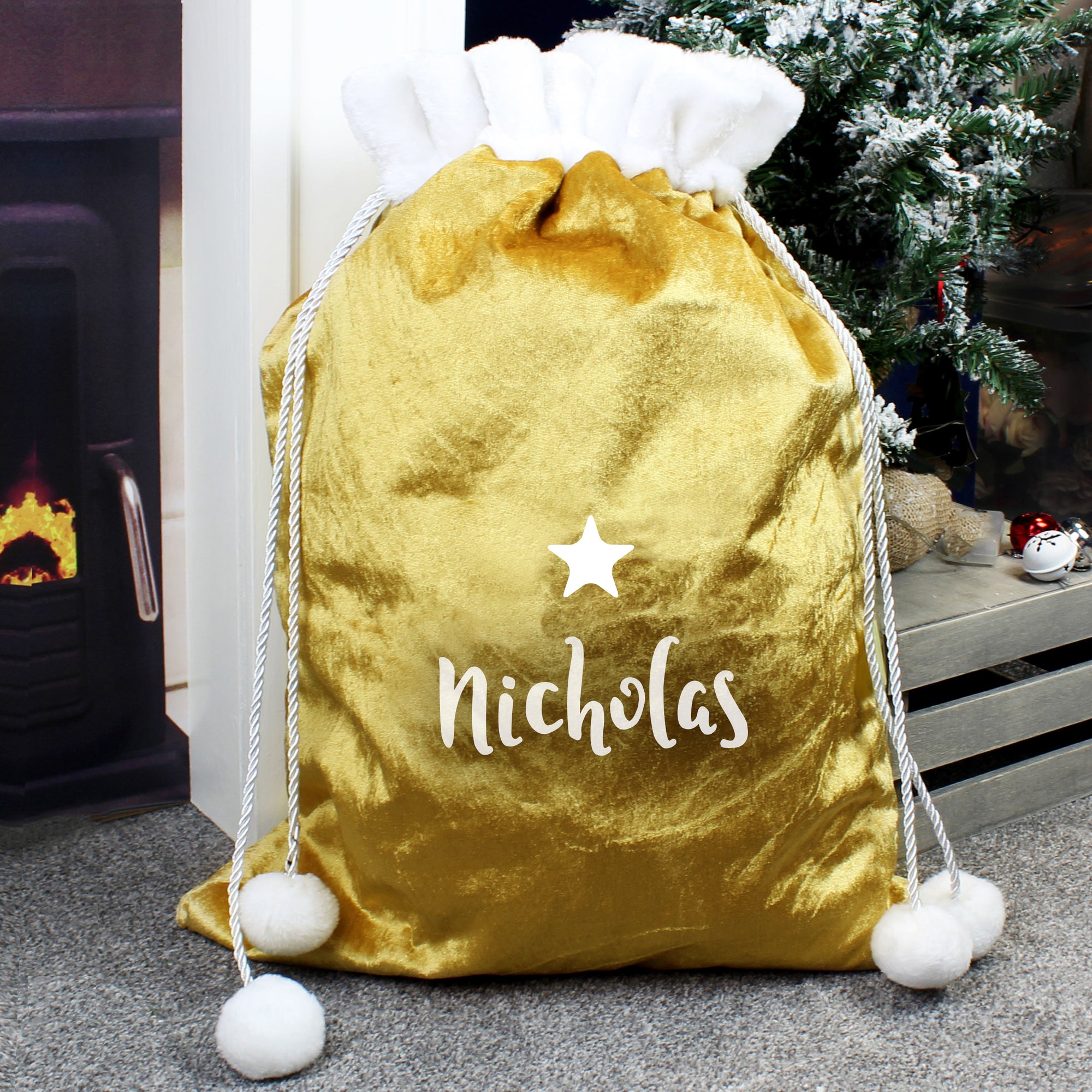 Personalised plush gold Christmas present sack with a white fur trim at the top. The sack has drawstrings to close it with white fur poms poms on the end. The front of the sack features a small white star and a name of your choice can be printed directly below it in a modern white cursive font.