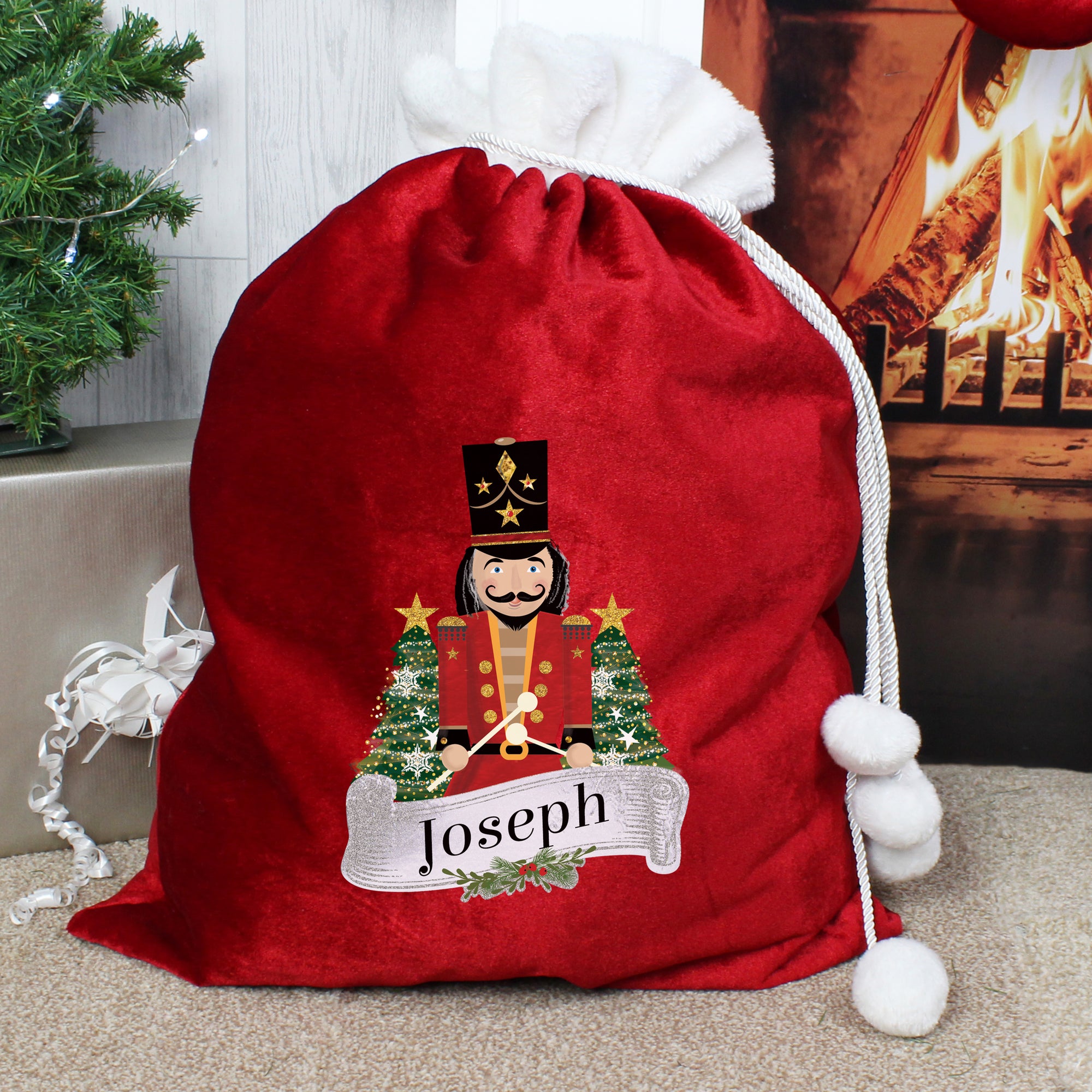 Personalised Christmas present sack made from plush red fleece fabric with a white fur collar. The bag has drawstrings to close it with white pom poms on the end and the front of the sack has an image of a wooden nutcracker toy on it and it can be personalised with a name of your choice of up to 12 characters.