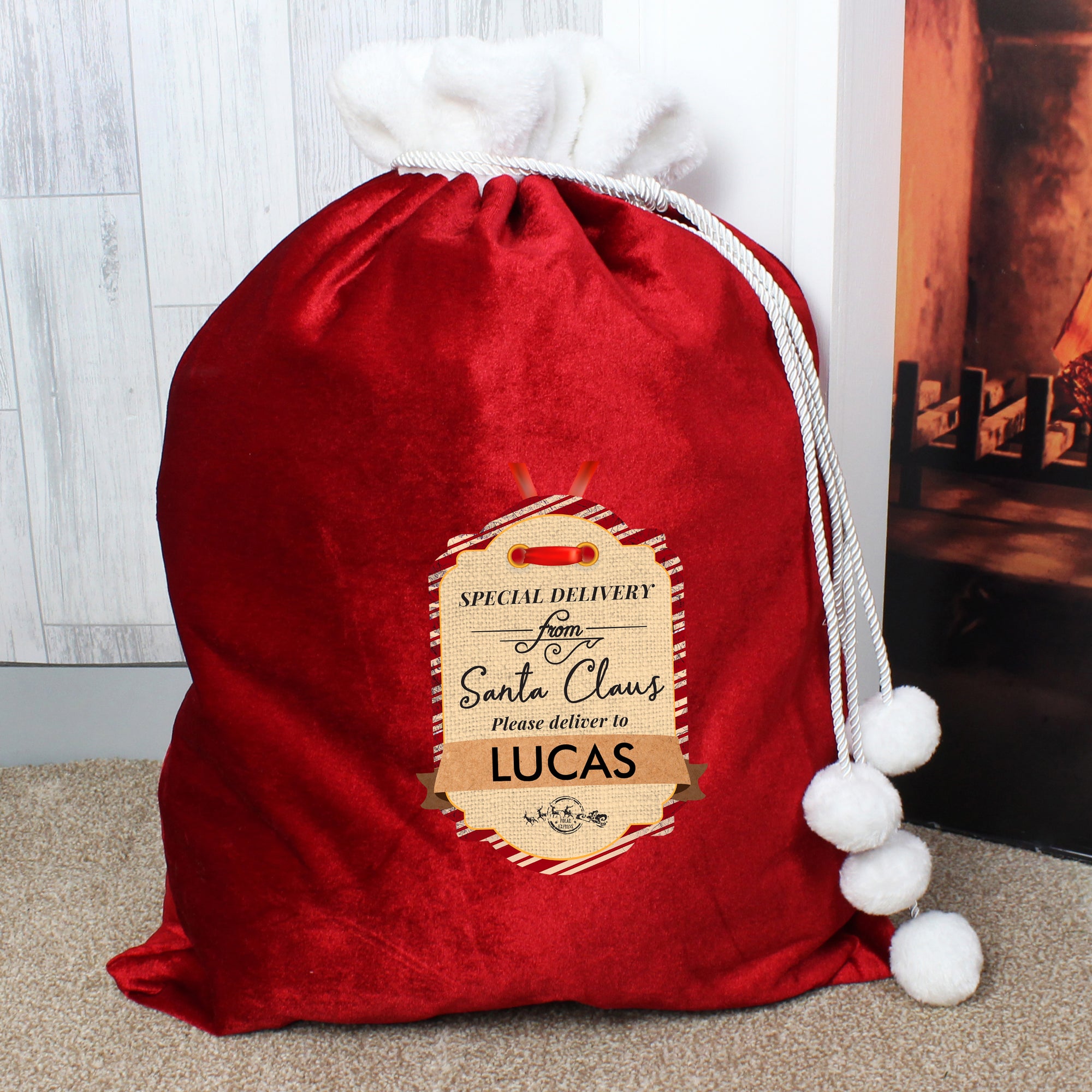 Personalised plush red Christmas gift sack with a white fur collar and white drawstrings with pom poms on the end. The front of the sack features a printed label that says 'Special delivery from Santa Claus. Please deliver to' and then you can add a name of your choice of up to 12 characters which will be printed in black uppercase.