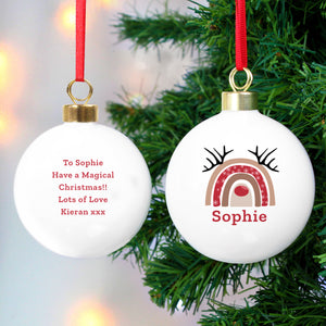 Image of the front and back of a personalised Christmas bauble. The bauble is white, the front features an image of a modern rainbow with a red nose in the middle and antlers on the top and below it you can add a name of your choice which will be printed in red text. You can add your own message to the back of the bauble which will be printed in the same matching red text as the front.
