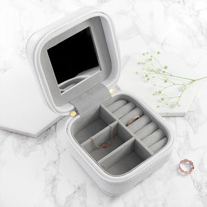 Image of a white leather square travel jewellery case that can be personalised with a name of your choice of up to 15 characters on the lid in a choice of colours and 3 different fonts. The case closes securely with a white zip and internally has flock lined compartments for storing jewellery.