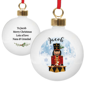 Personalised Christmas bauble featuring an image of a hand drawn wooden nutcracker toy with a drum. A name of your choice will be printed above the image in a black modern cursive font. The rear of the bauble can be personalised with your own special message over up to 4 lines. The bauble comes ready to hang with a ribbon